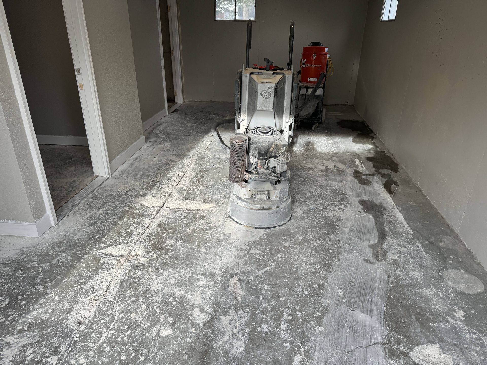 Concrete floor being ground with a large industrial machine in a room with light-colored walls.