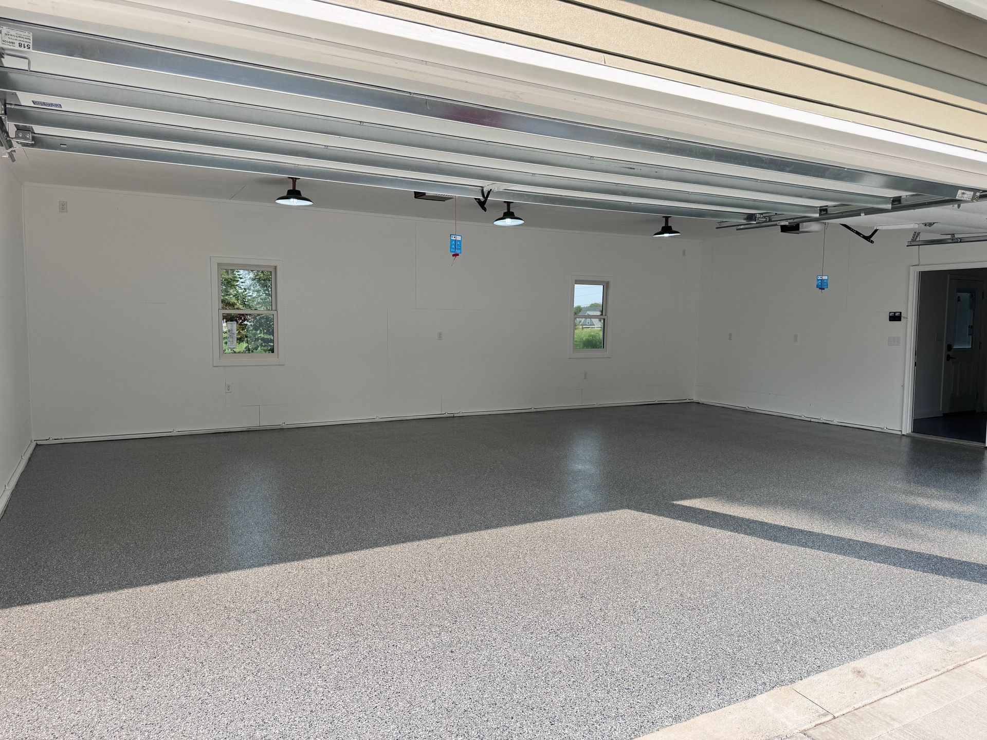 Empty garage with epoxy floor, white walls, two windows, and overhead lights.