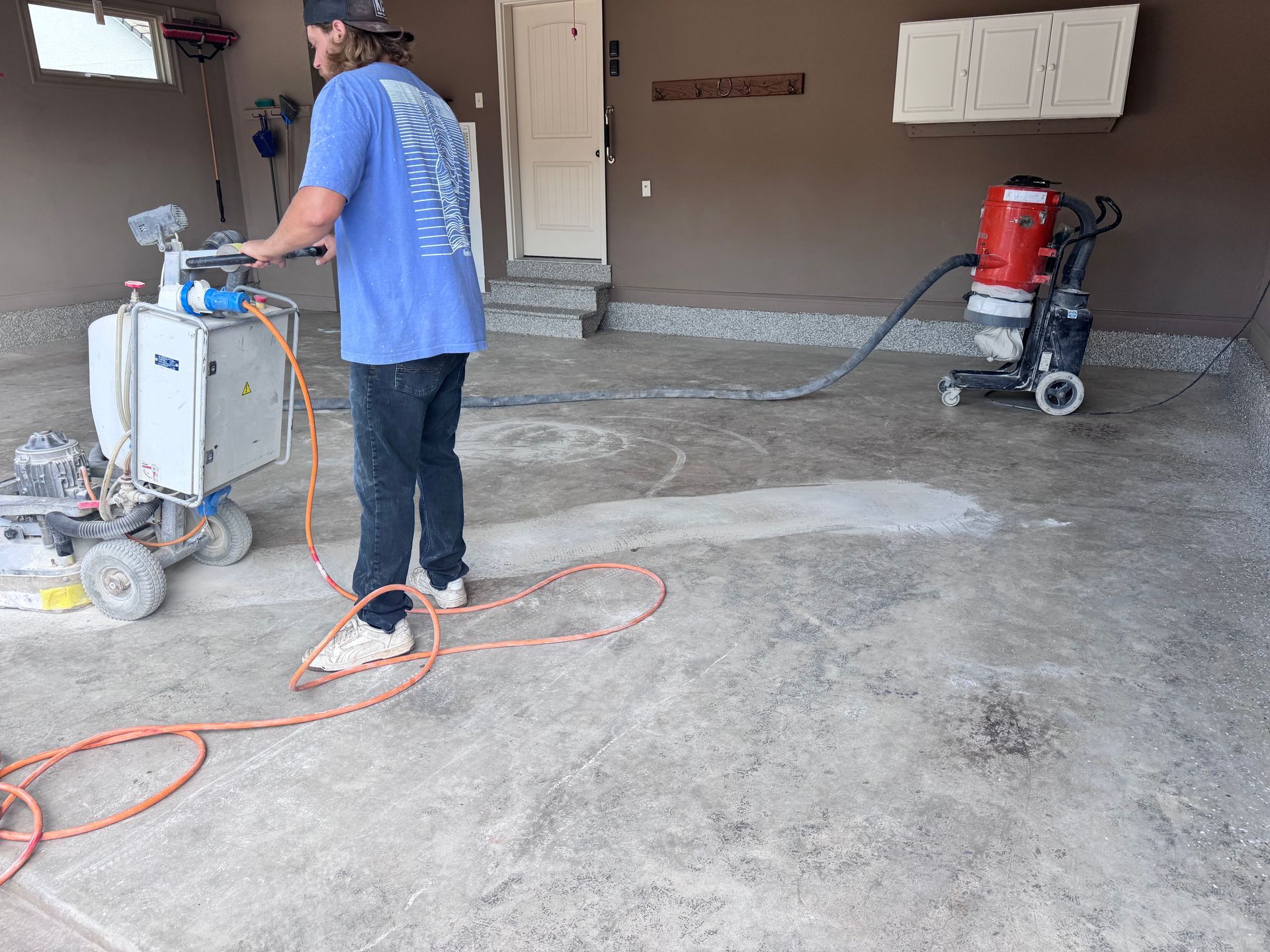 Man using a floor grinder in a garage; equipment attached to a dust collector.