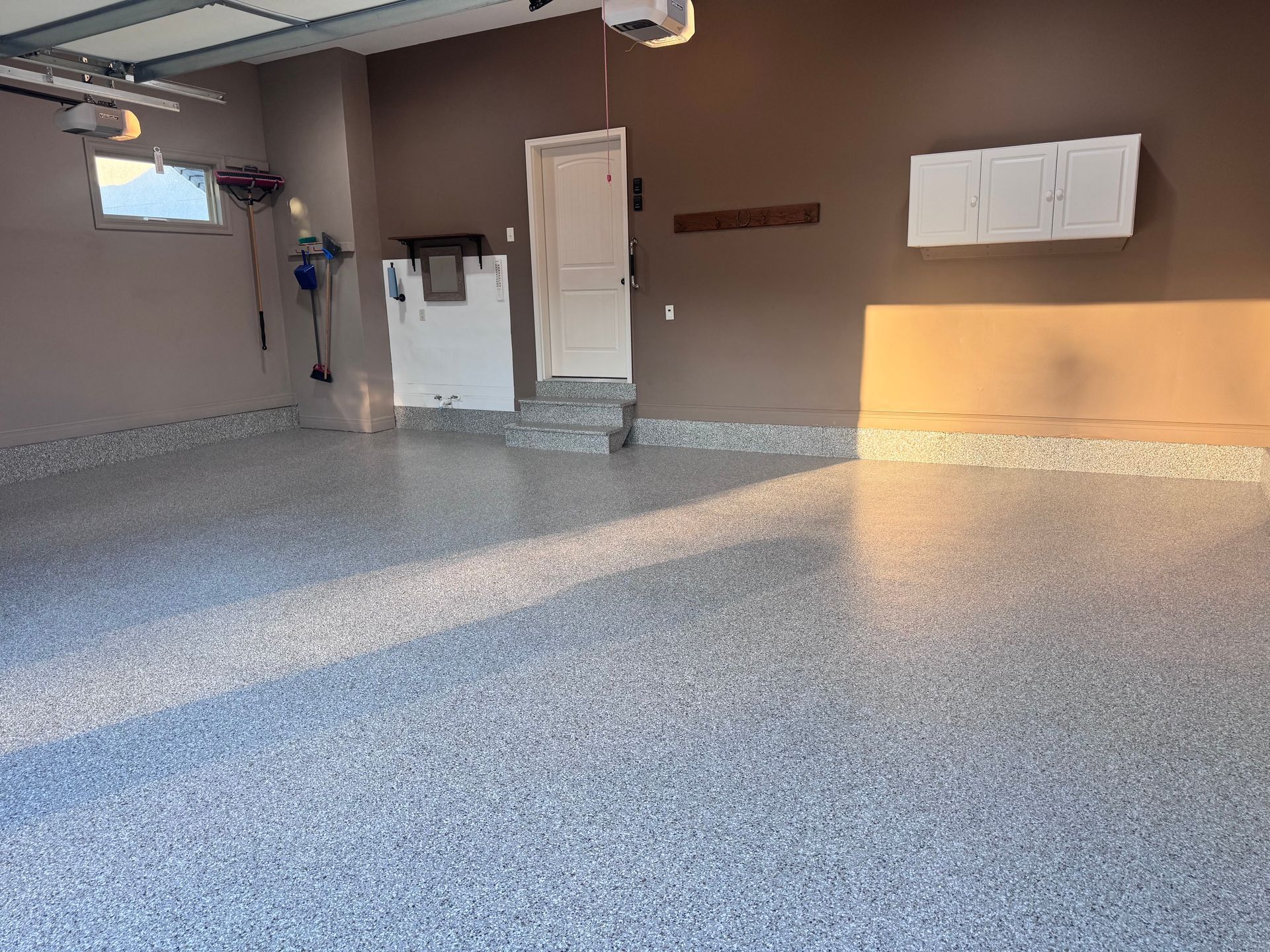 Empty garage with speckled epoxy floor, brown walls, and white storage cabinets.