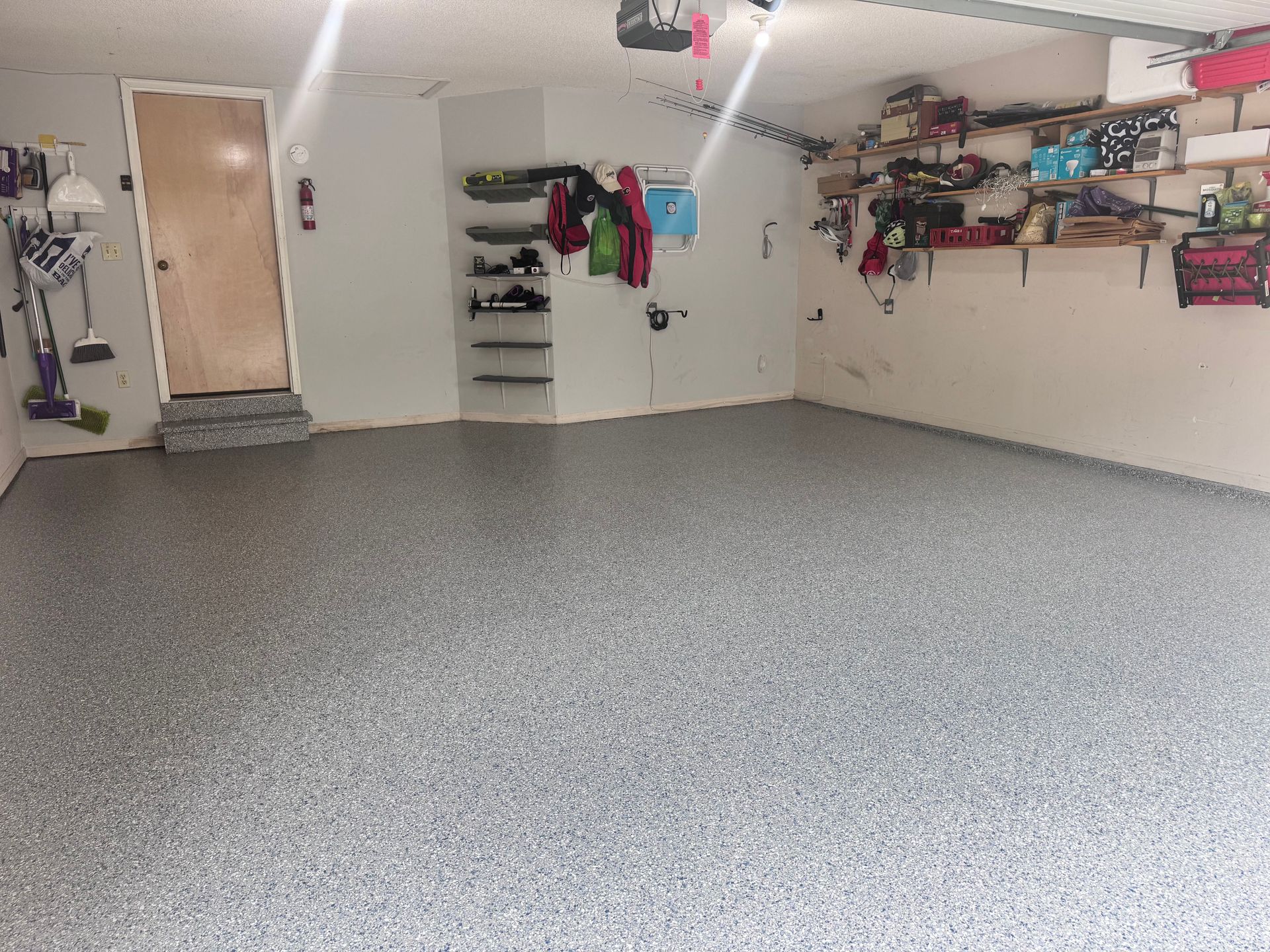Garage with gray speckled epoxy floor, shelves with items, door, and storage.