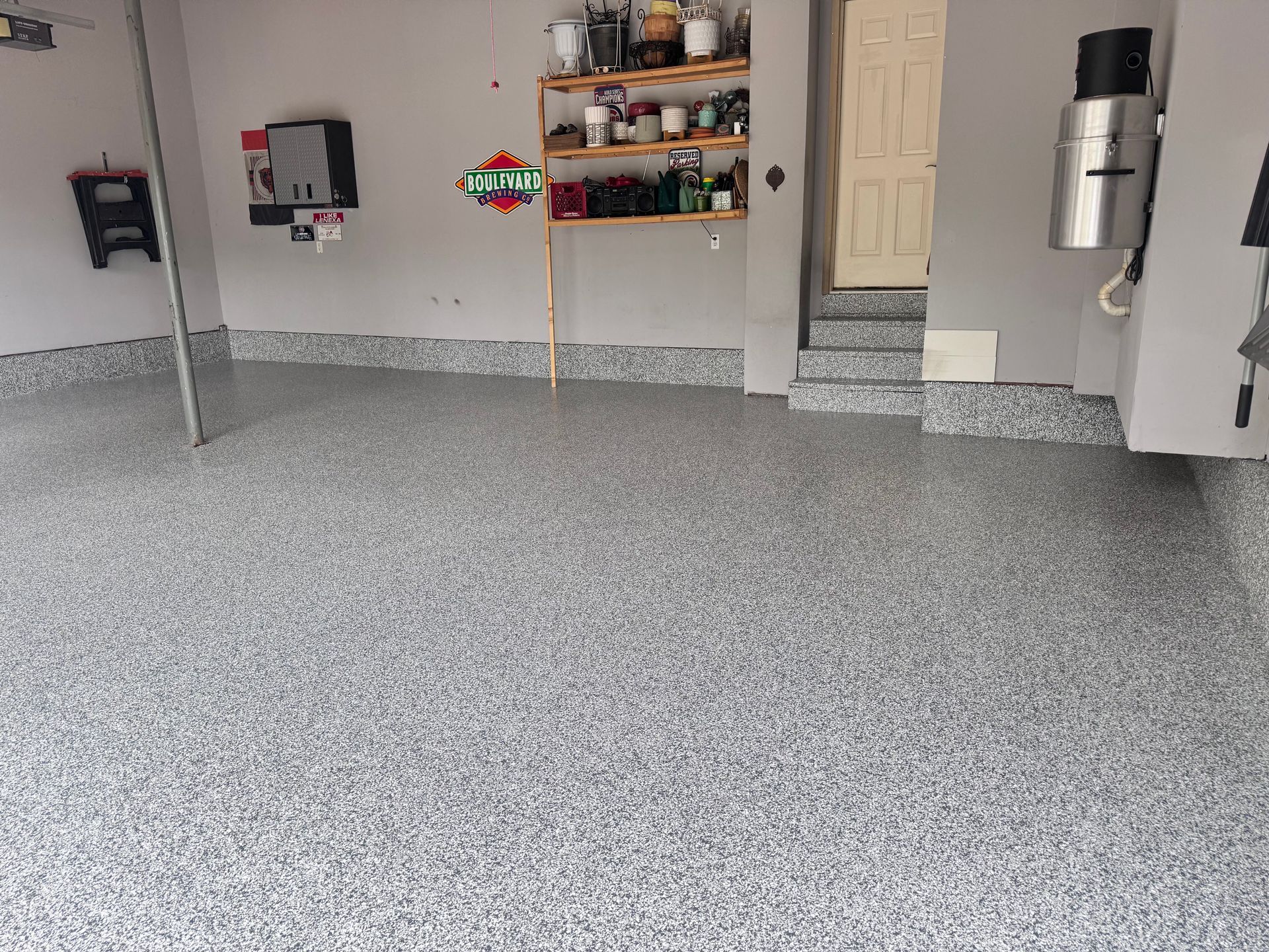 Garage with speckled gray epoxy flooring, shelves of items, and a door.