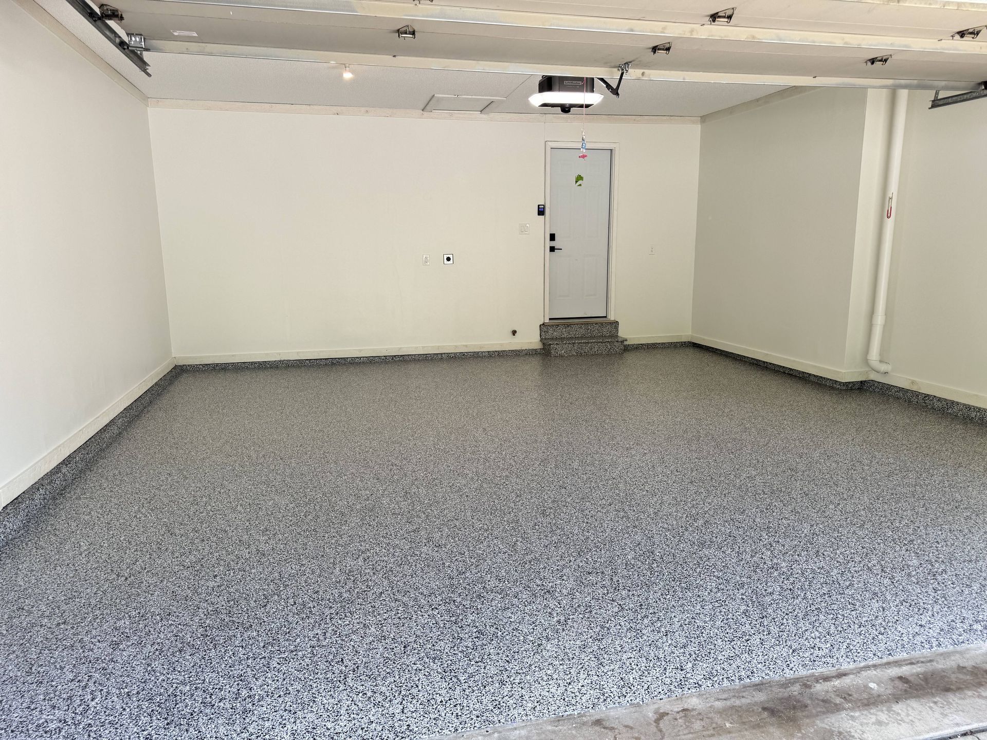 Empty garage with gray speckled epoxy floor and white walls. A door is visible in the back.