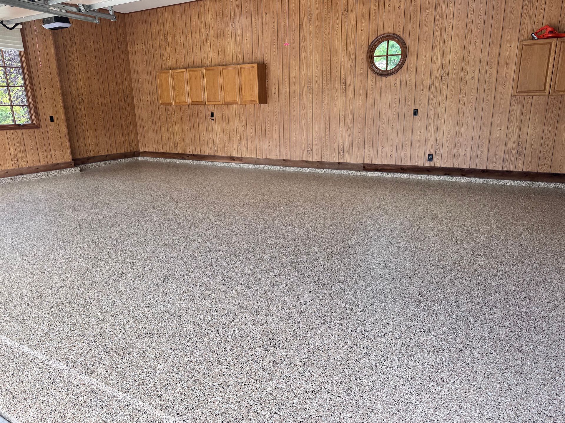 Garage interior with speckled epoxy floor, wooden walls, and a round window.