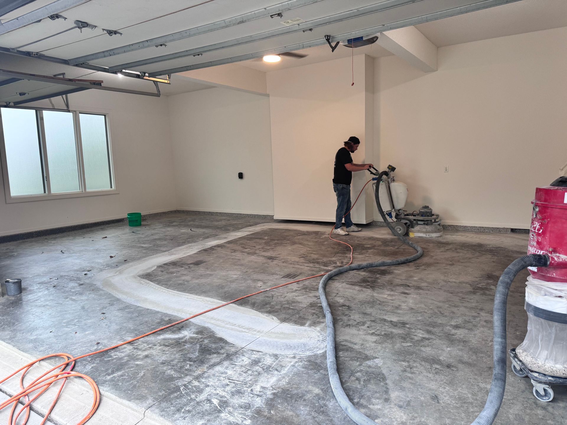 Person using a machine to grind a garage floor, dust collection system attached.