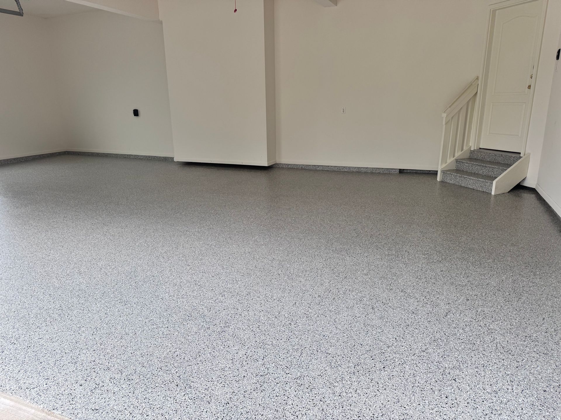 Garage interior with gray speckled epoxy floor and white walls. Stairs on the right.