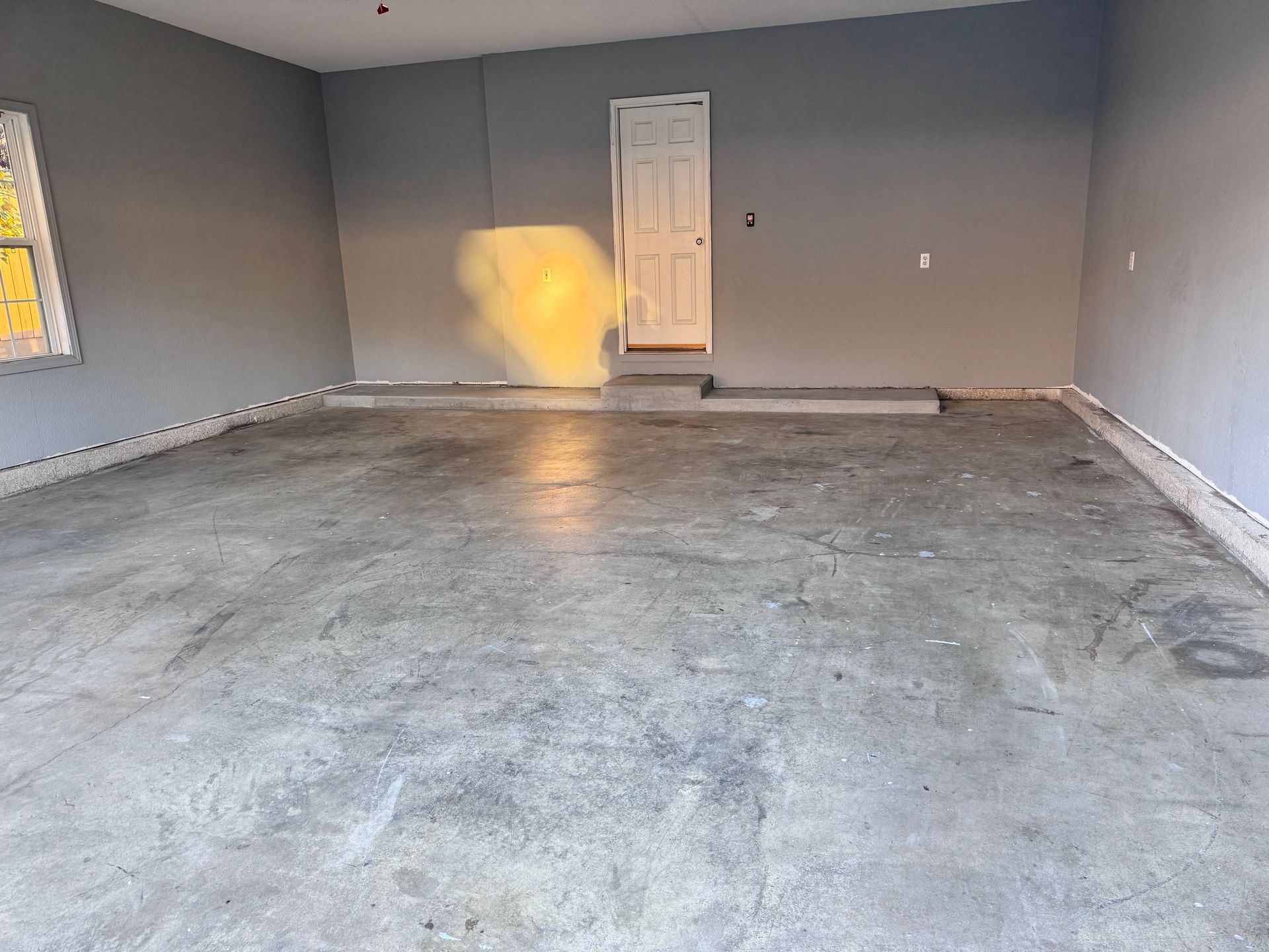 Empty garage with gray walls, concrete floor, and white door.