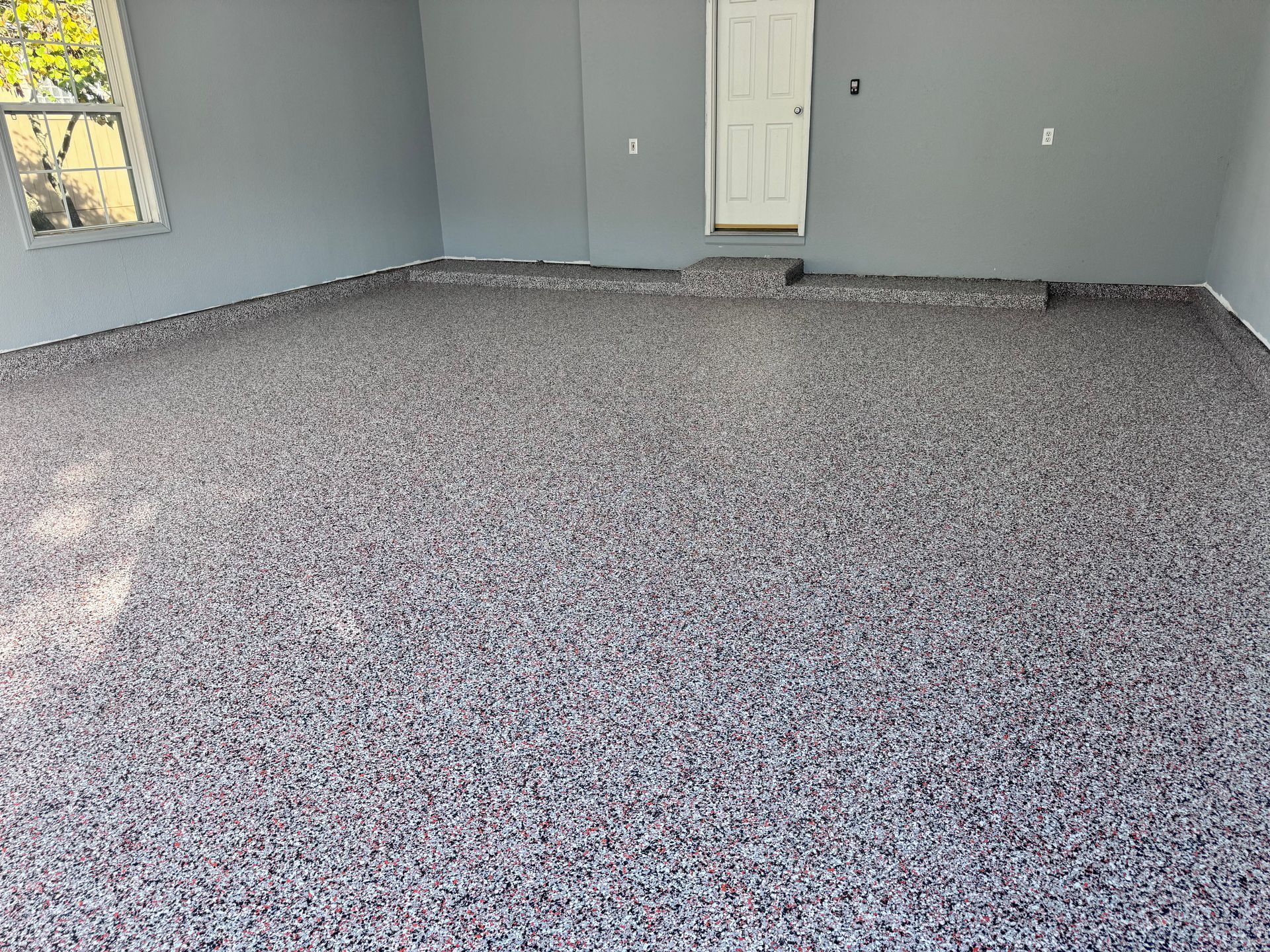 Garage floor coated in epoxy with decorative flakes, in front of a gray door and walls.