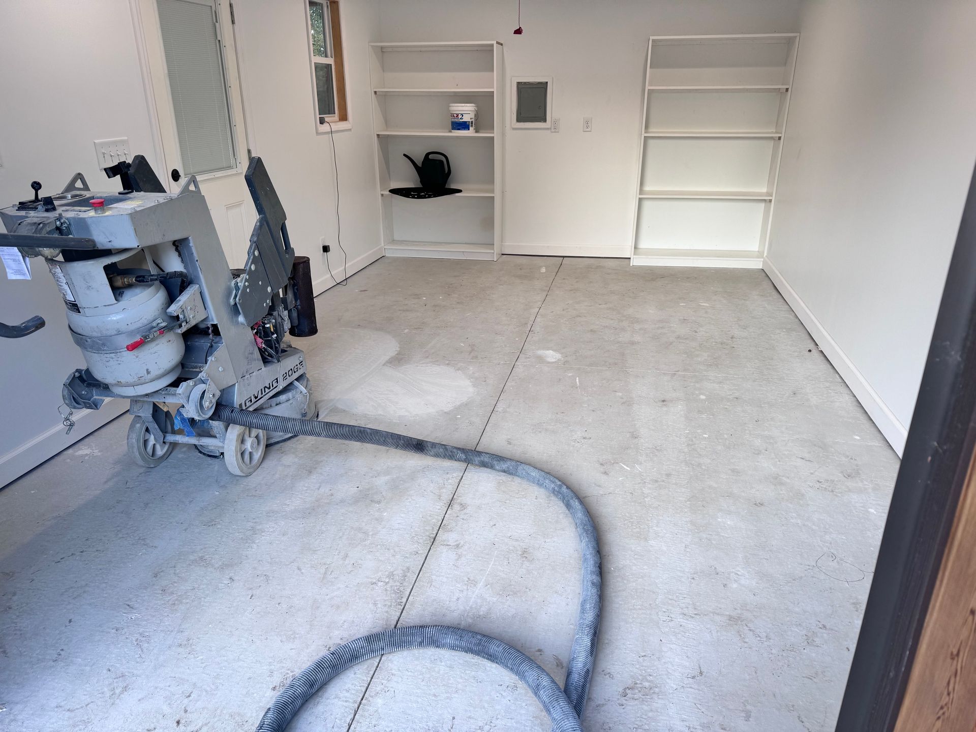 Concrete floor grinding in a room with white walls and built-in shelving; grinding machine is present.