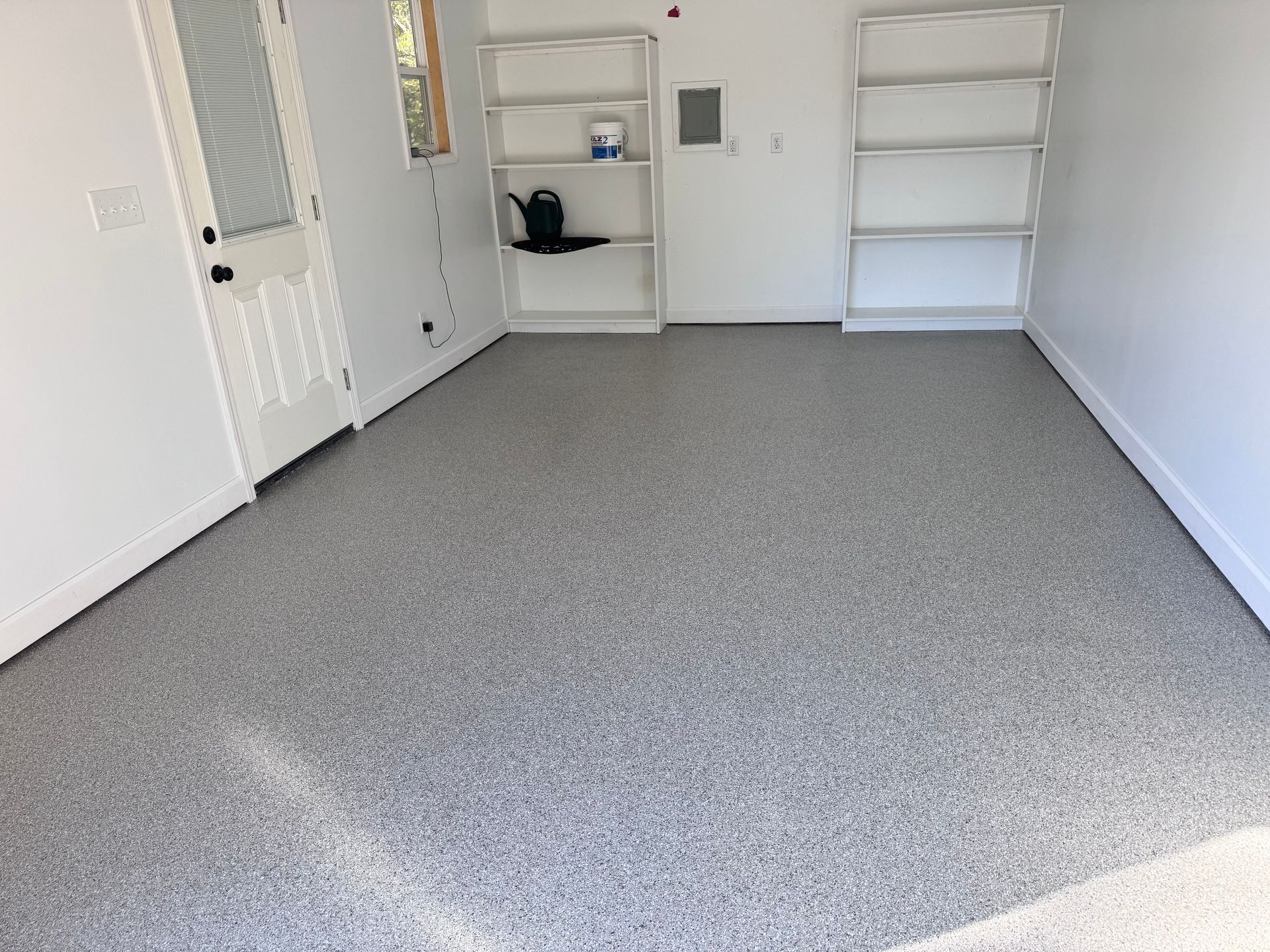 Gray speckled epoxy garage floor. White walls, shelves, and door; neutral lighting.