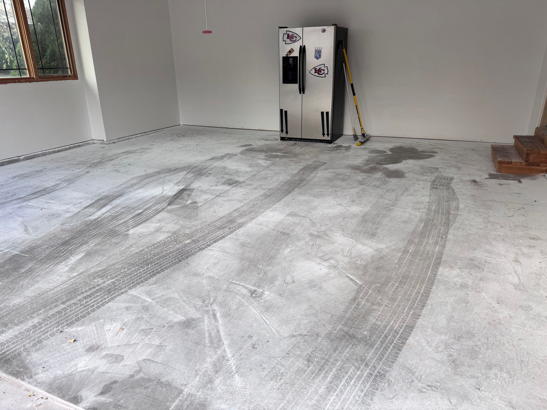Concrete floor with tire tracks, a refrigerator, and tools in a room with white walls and a window.
