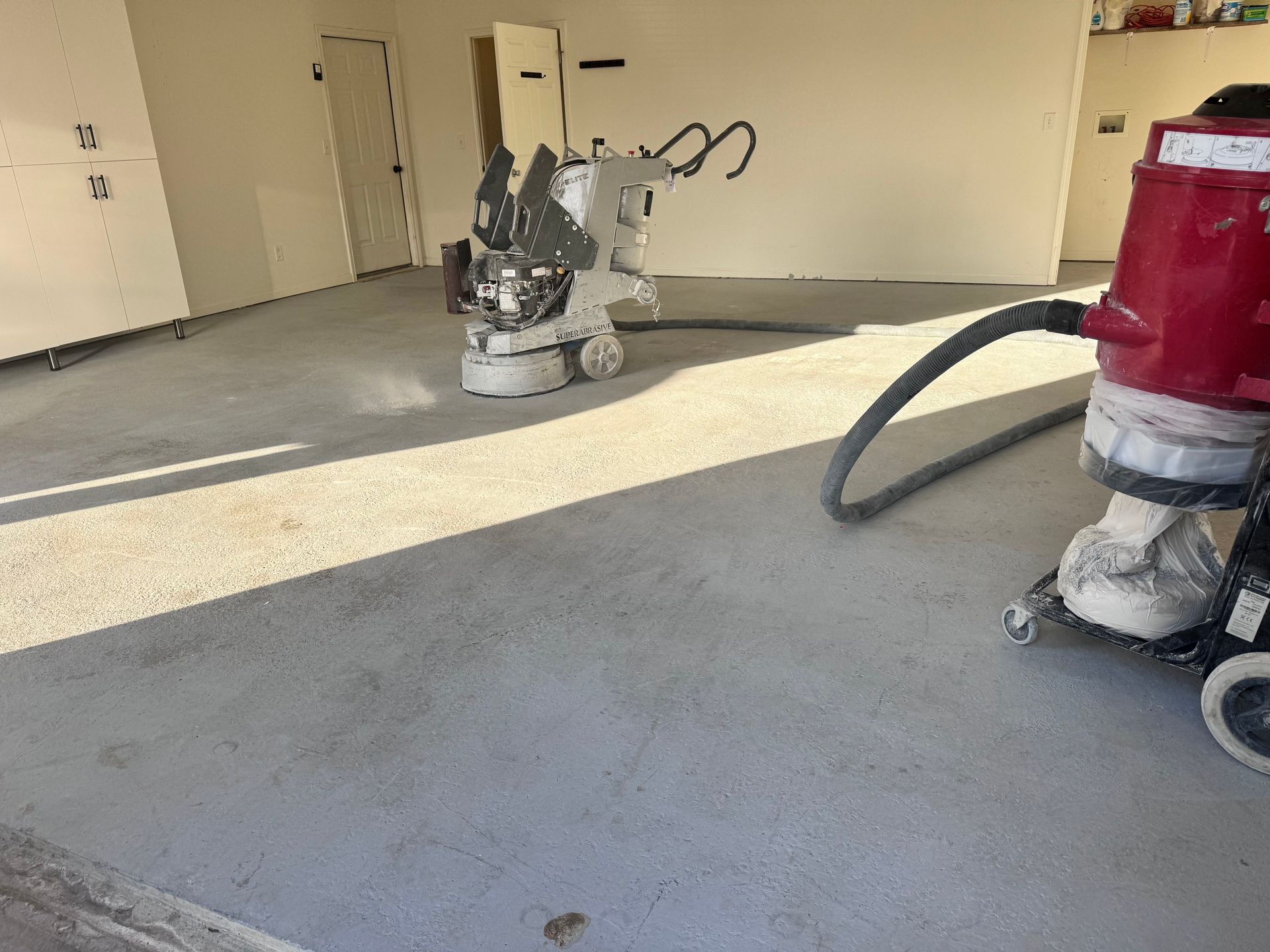 Concrete floor being ground with machinery, creating dust in an interior room.