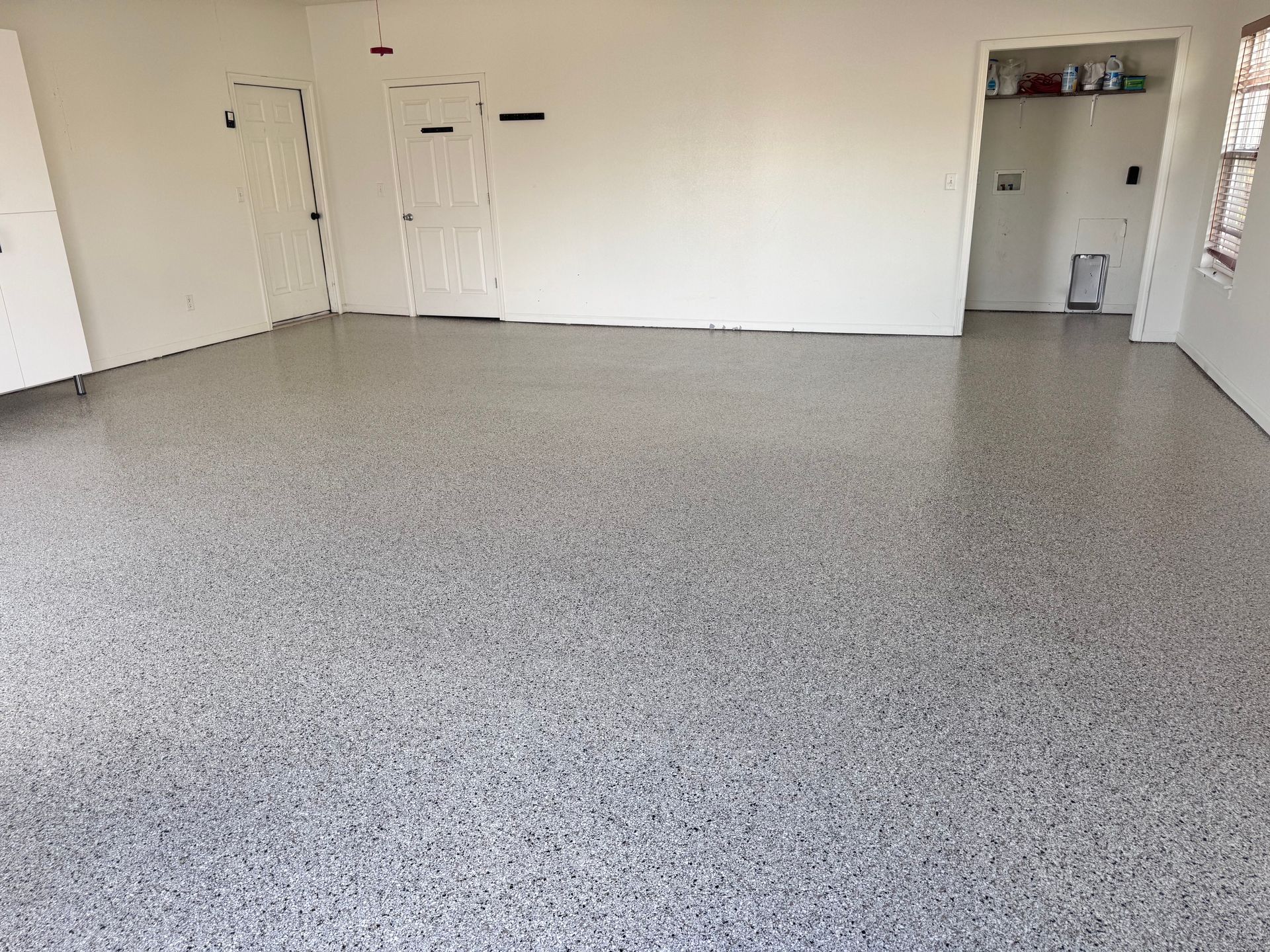 Garage with speckled gray epoxy flooring, white walls, and closed doors.