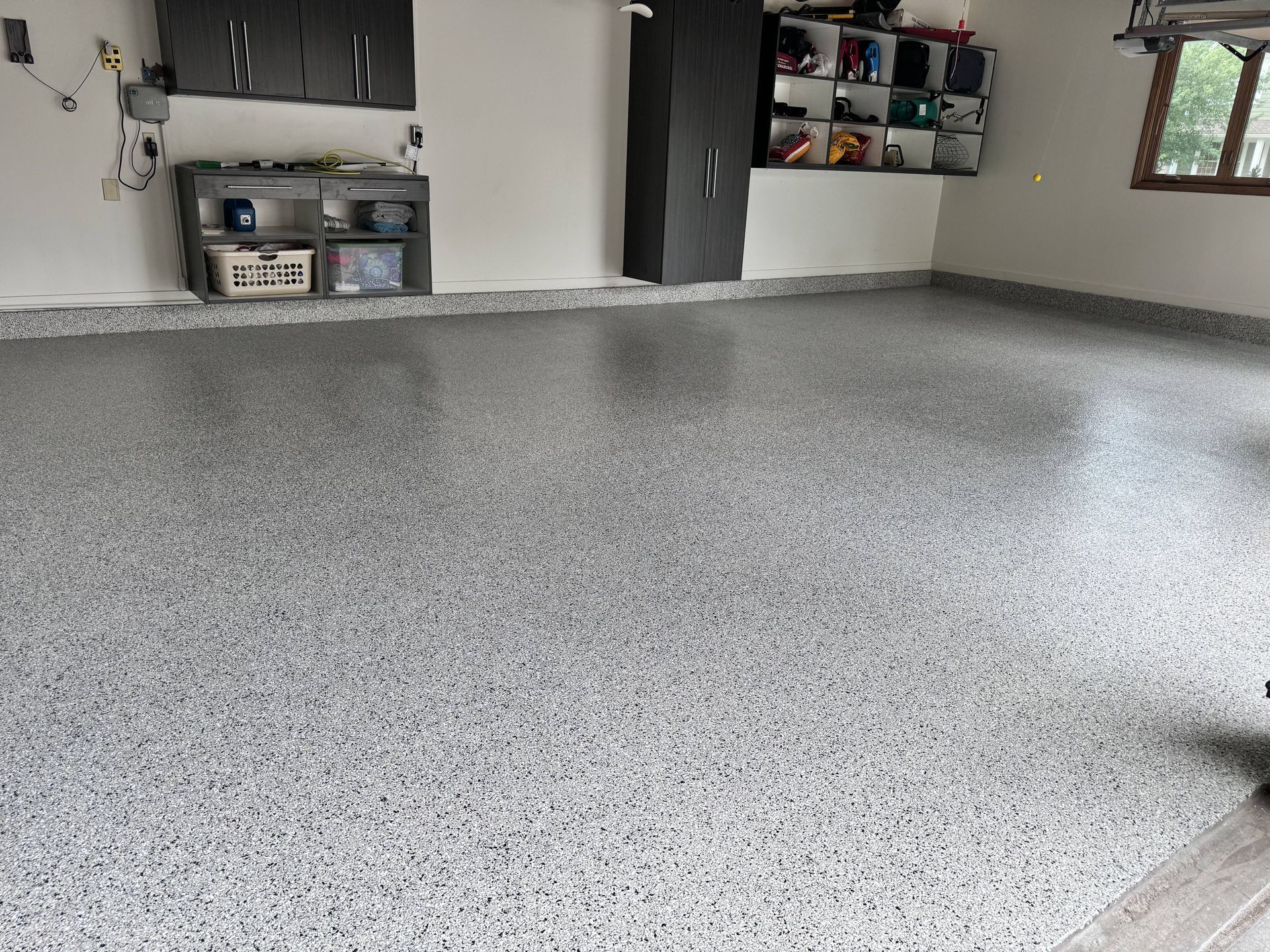 A garage with a gray speckled epoxy floor, cabinets, and storage shelves.