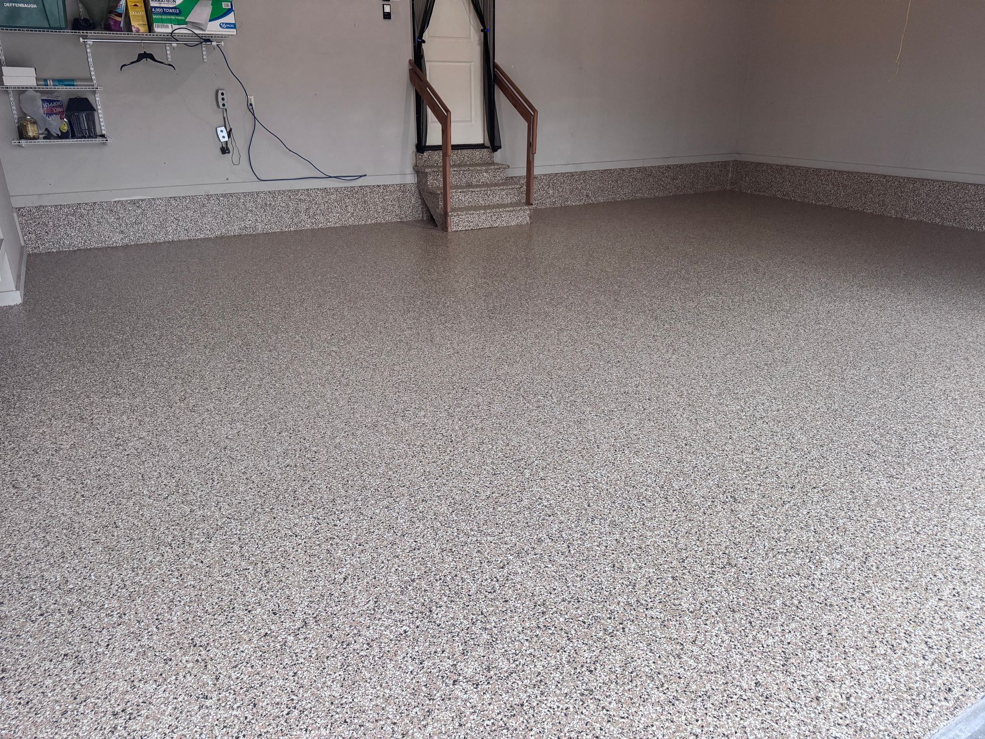 Garage with a speckled epoxy floor. A set of stairs leads up to a door.