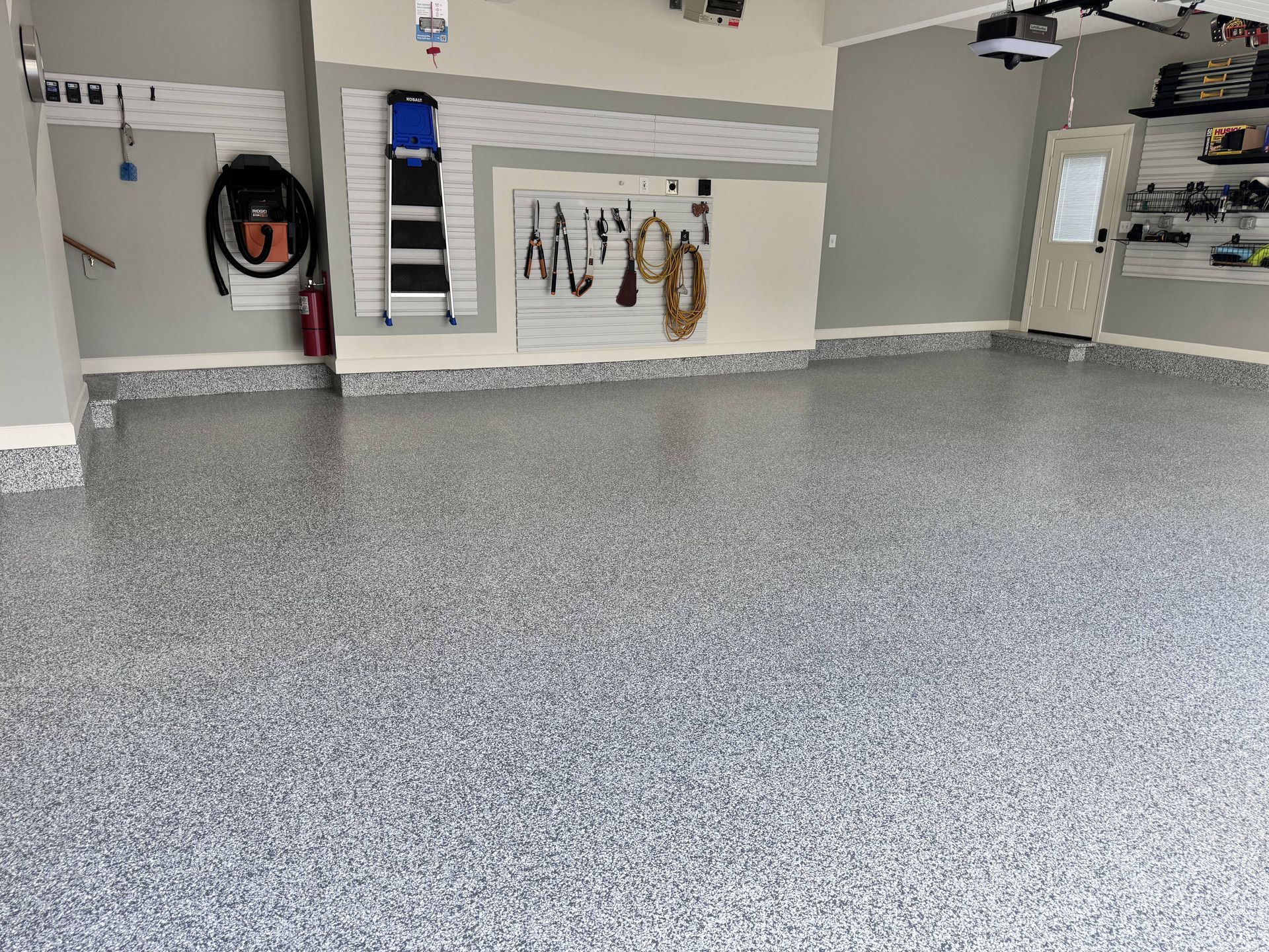 Garage with a gray and white speckled epoxy floor, tools on the wall, and a door.