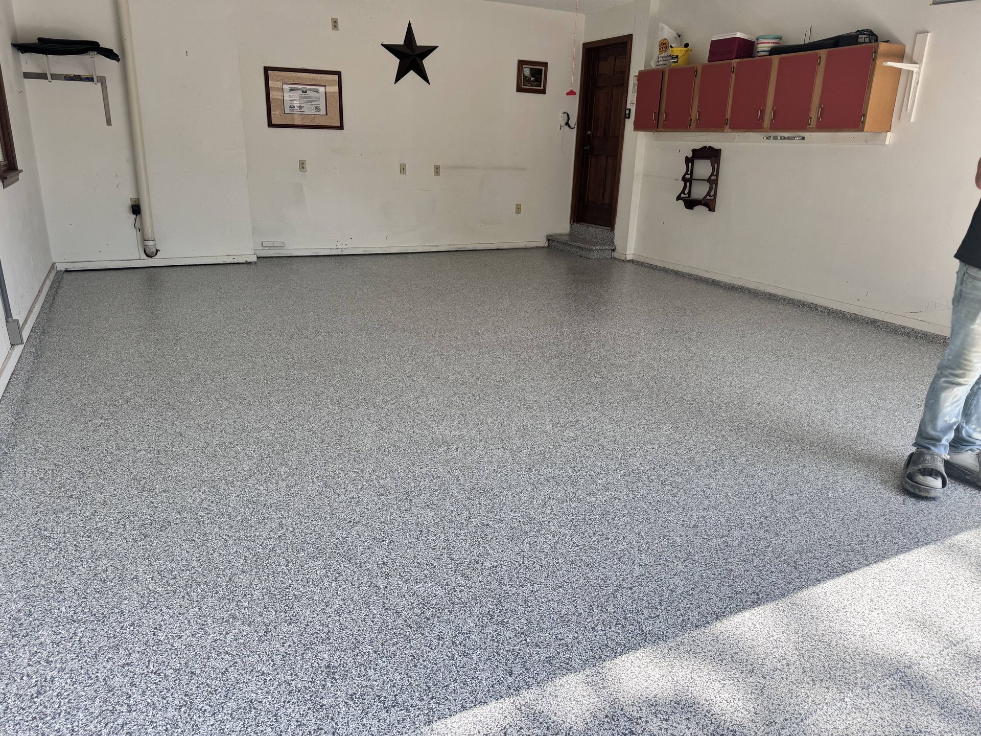 Garage with a speckled epoxy floor, white walls, and a person standing in the corner.
