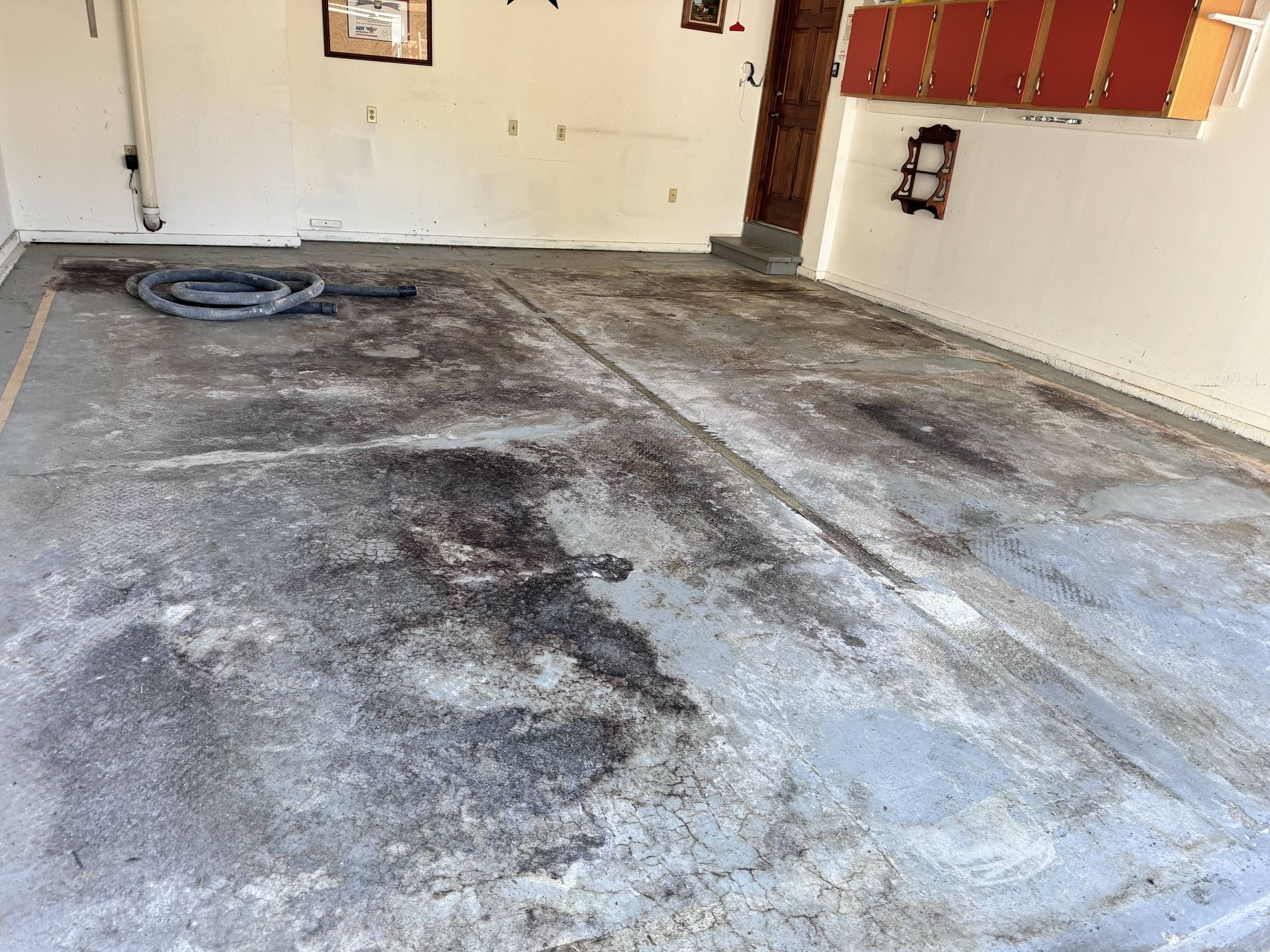 Garage floor with dark stains, hose, and off-white walls.