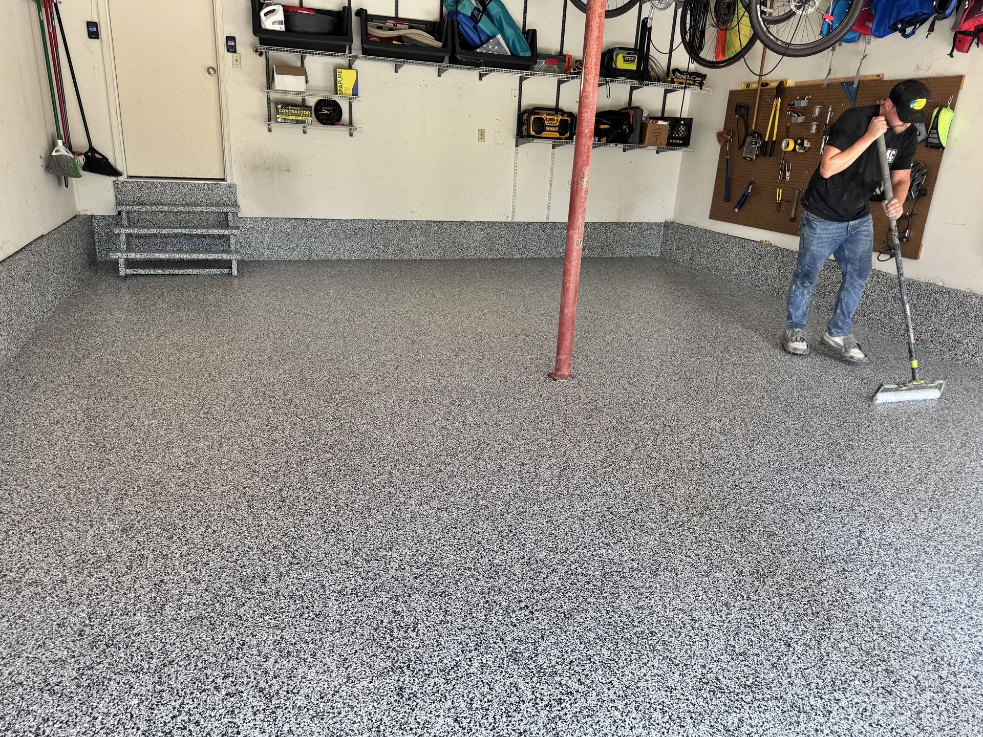Garage with epoxy floor, man sweeping. Tools and bikes on wall.