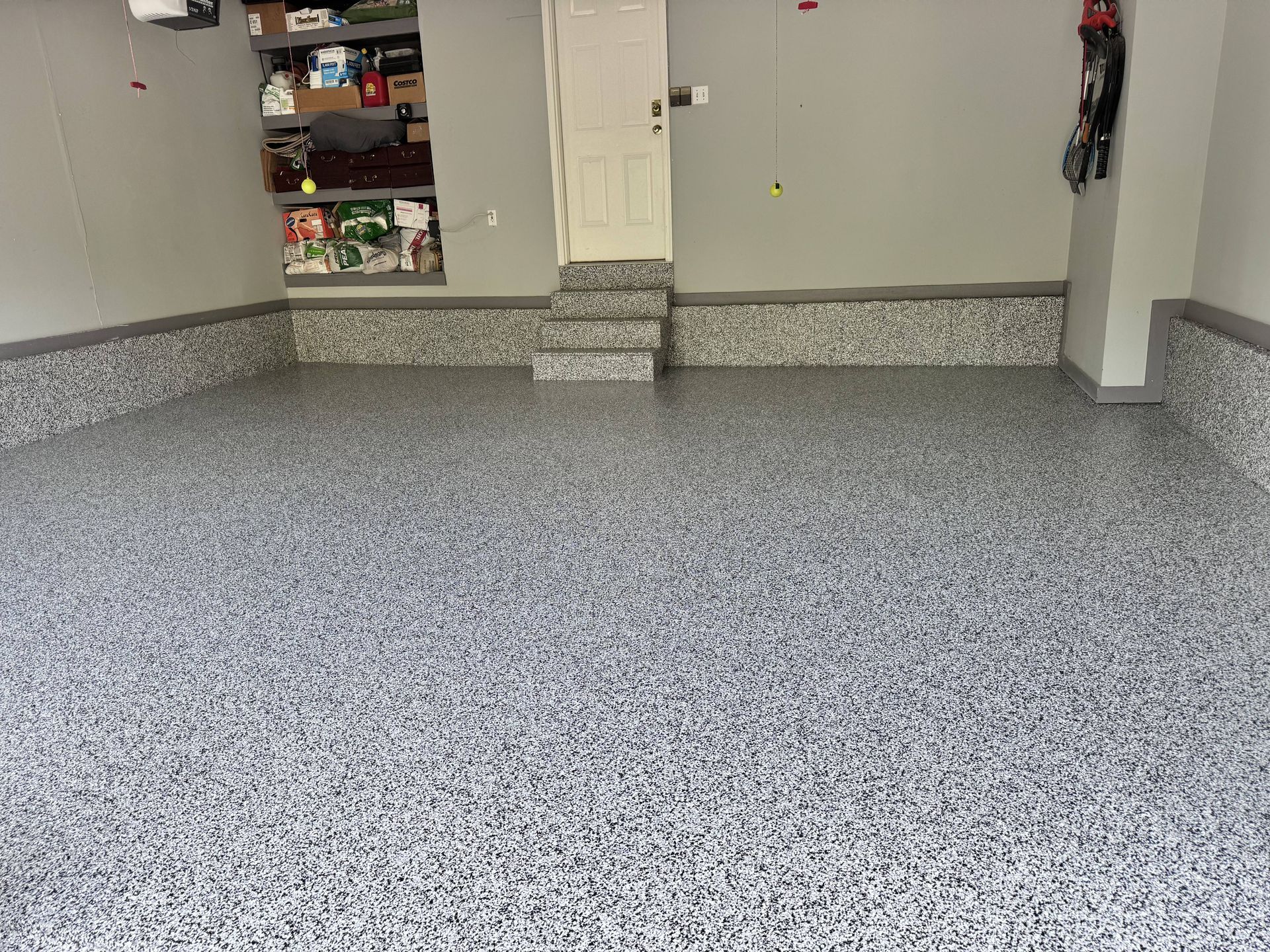 Garage with speckled, gray epoxy floor and steps leading to a white door.
