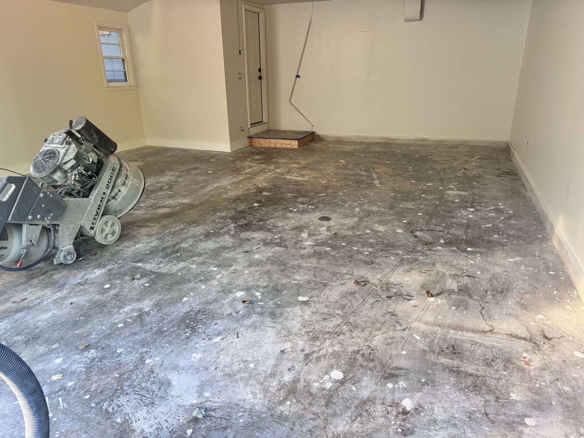 Concrete floor being ground down by a large machine in a room with light-colored walls.