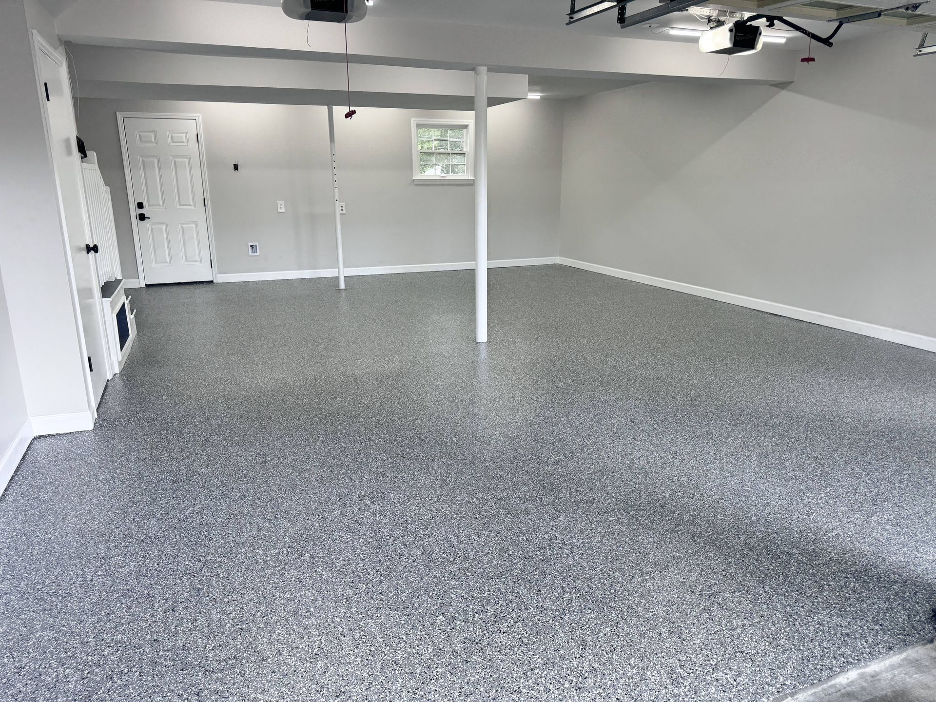 Garage with gray speckled epoxy floor and gray walls. Door, window, and support beams visible.