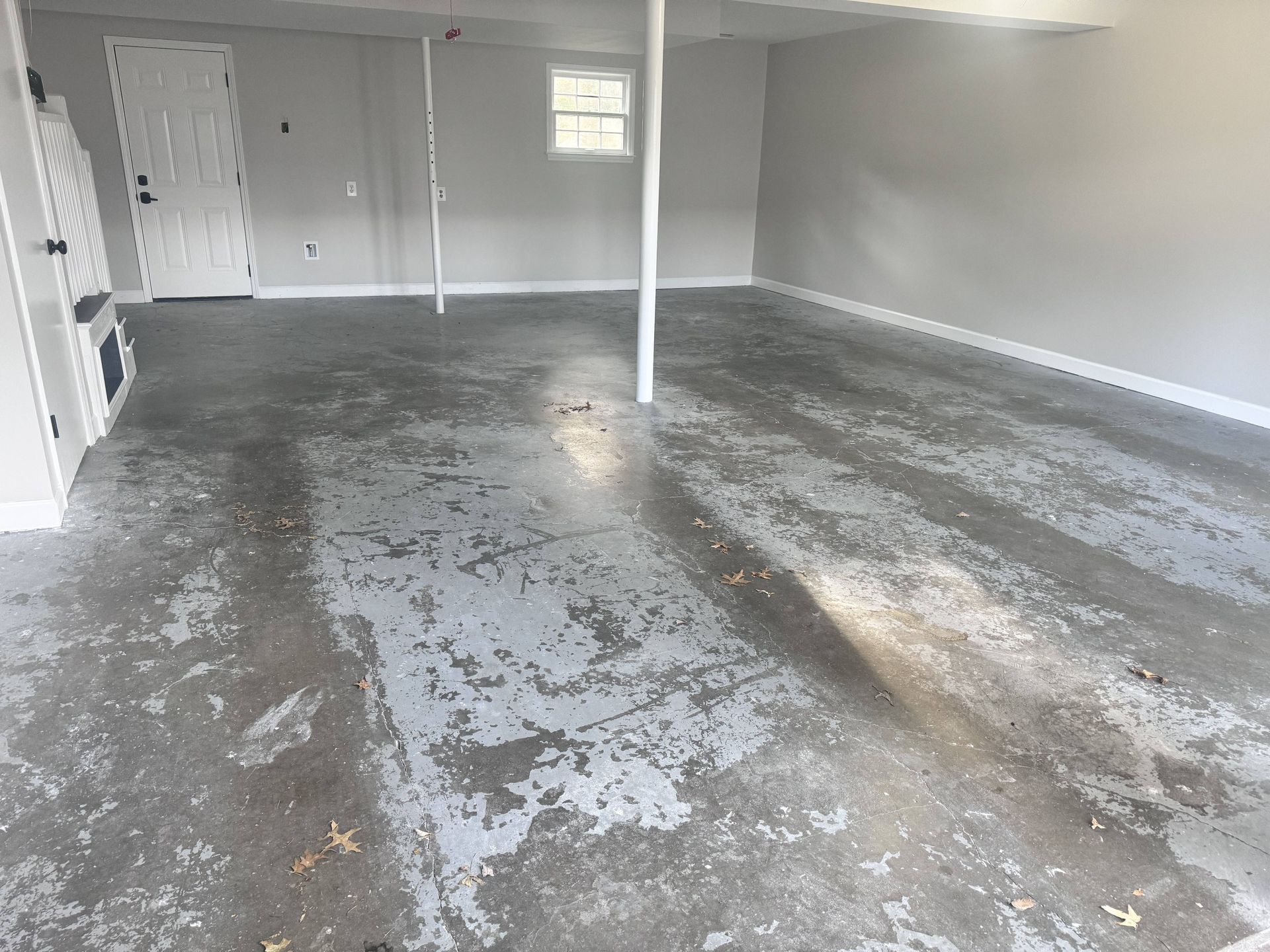 Garage interior with peeling gray floor paint, white walls, door, and a small window.