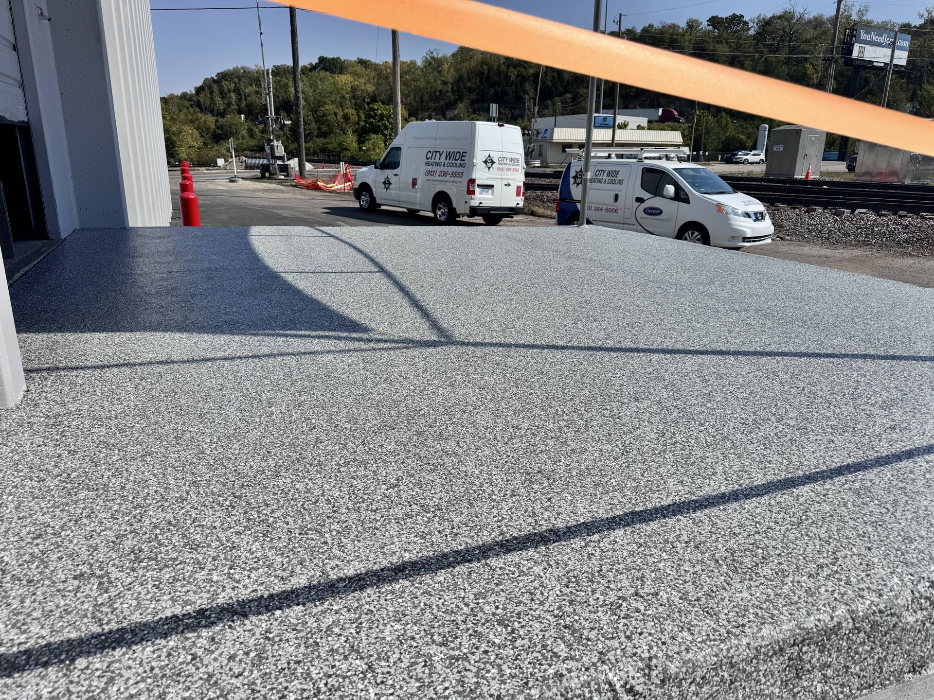 A newly paved, speckled-gray surface in front of a building; two service vans are parked nearby.