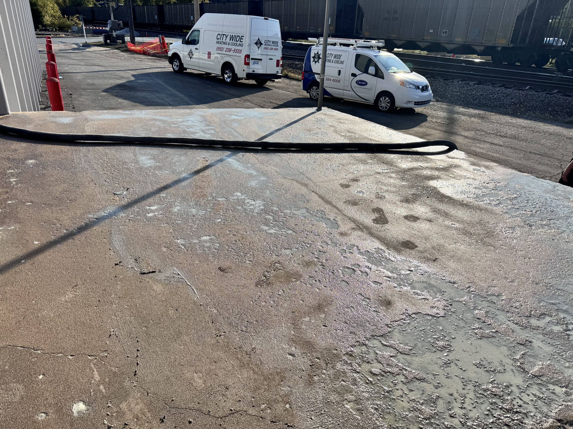 Two white vans, possibly utility vehicles, on asphalt near a building. A black hose lies on the ground.