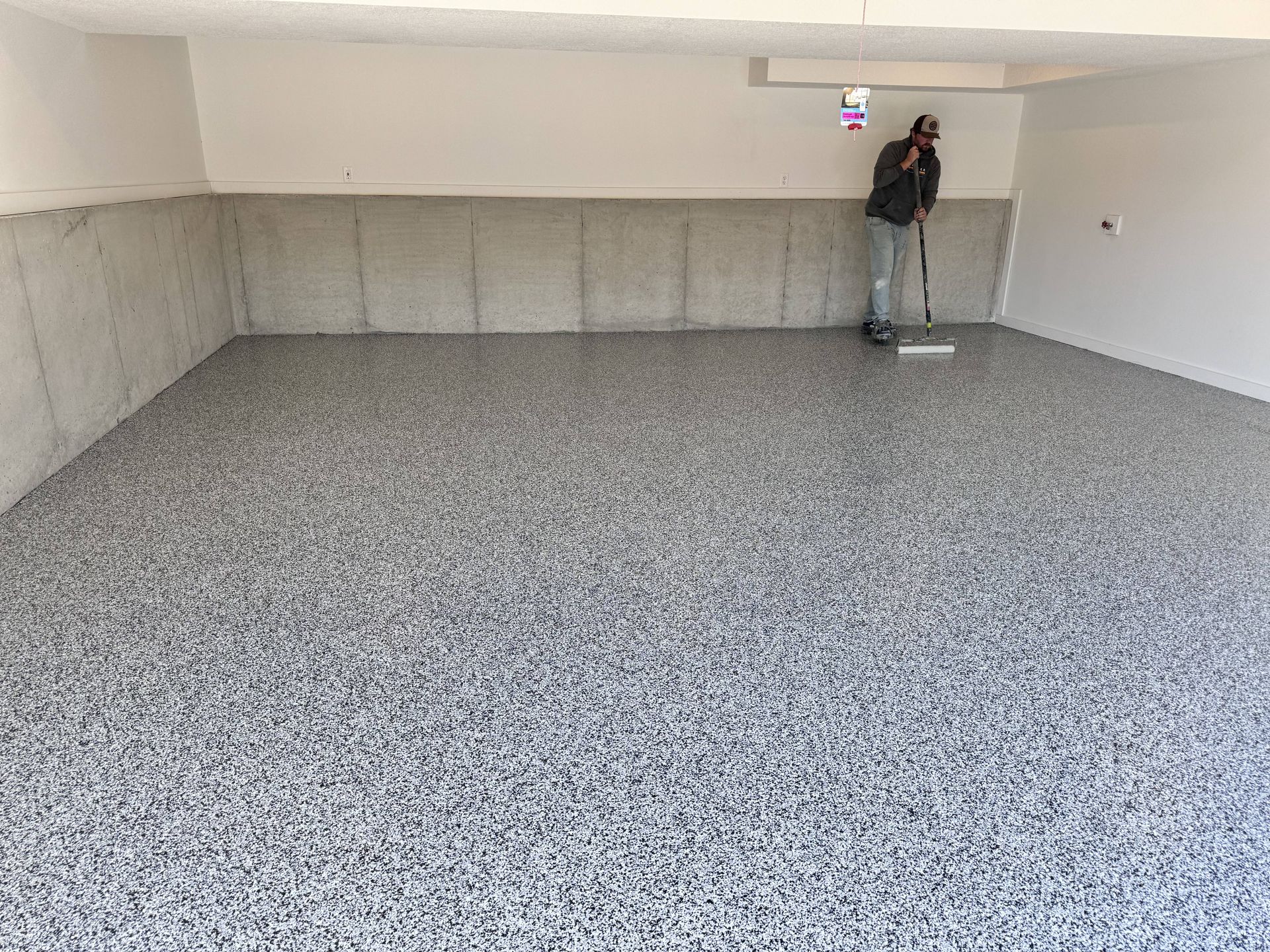 Man coating a garage floor with speckled gray epoxy.