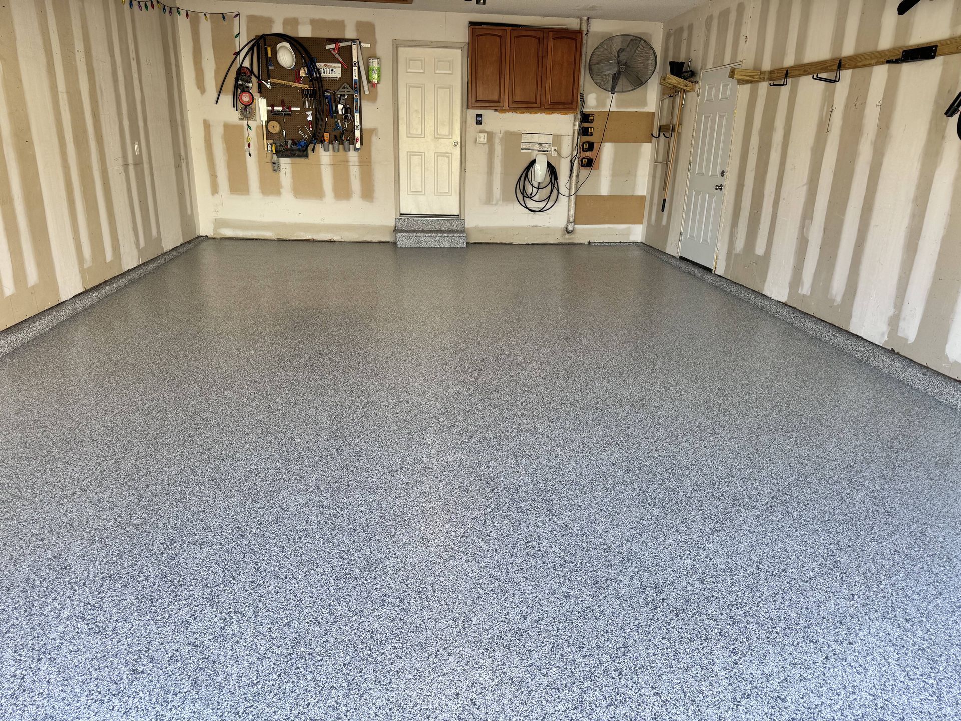 Garage with speckled gray epoxy flooring, tools, a door, and beige walls.