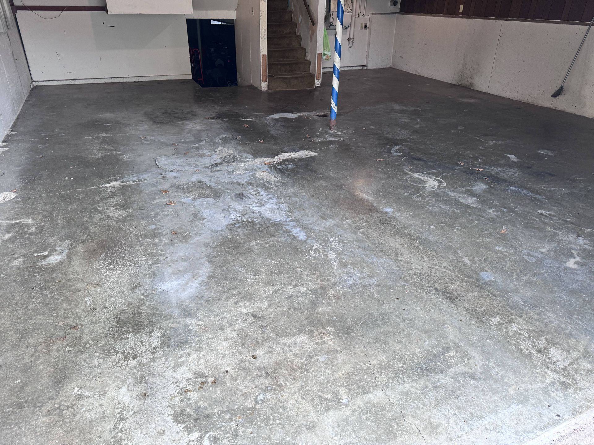 Concrete basement floor with stairs and a support pole in the background. Areas of water visible.
