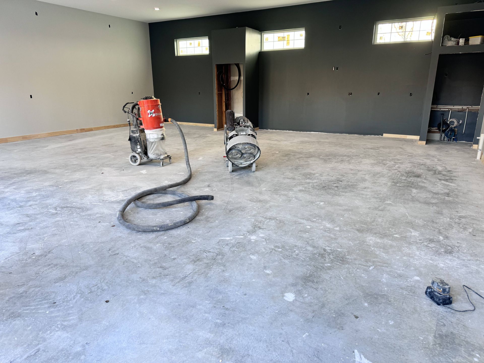 Concrete floor grinding equipment inside a room with gray walls, undergoing renovation.