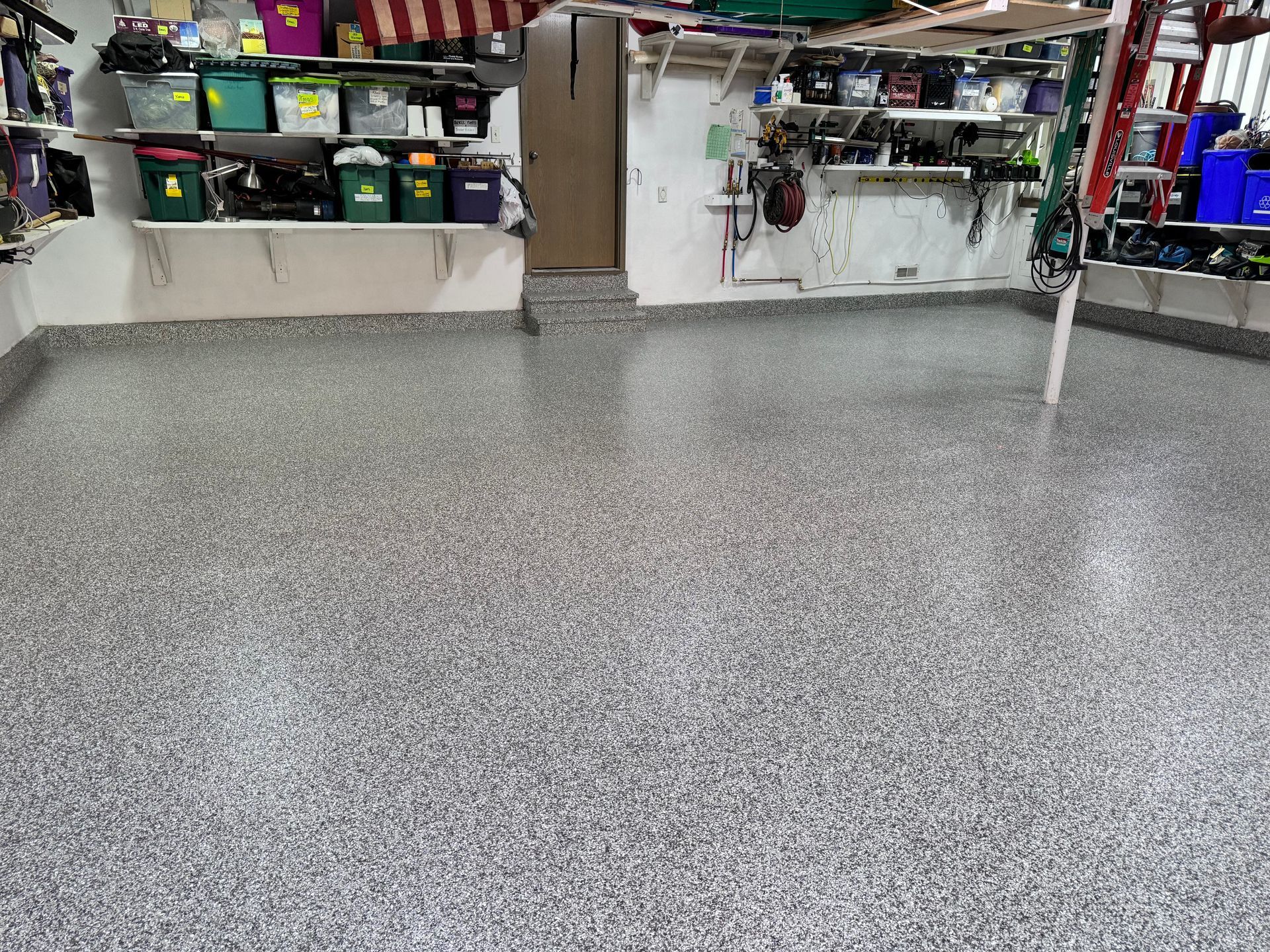 Garage with a gray speckled epoxy floor and shelves holding tools and supplies.