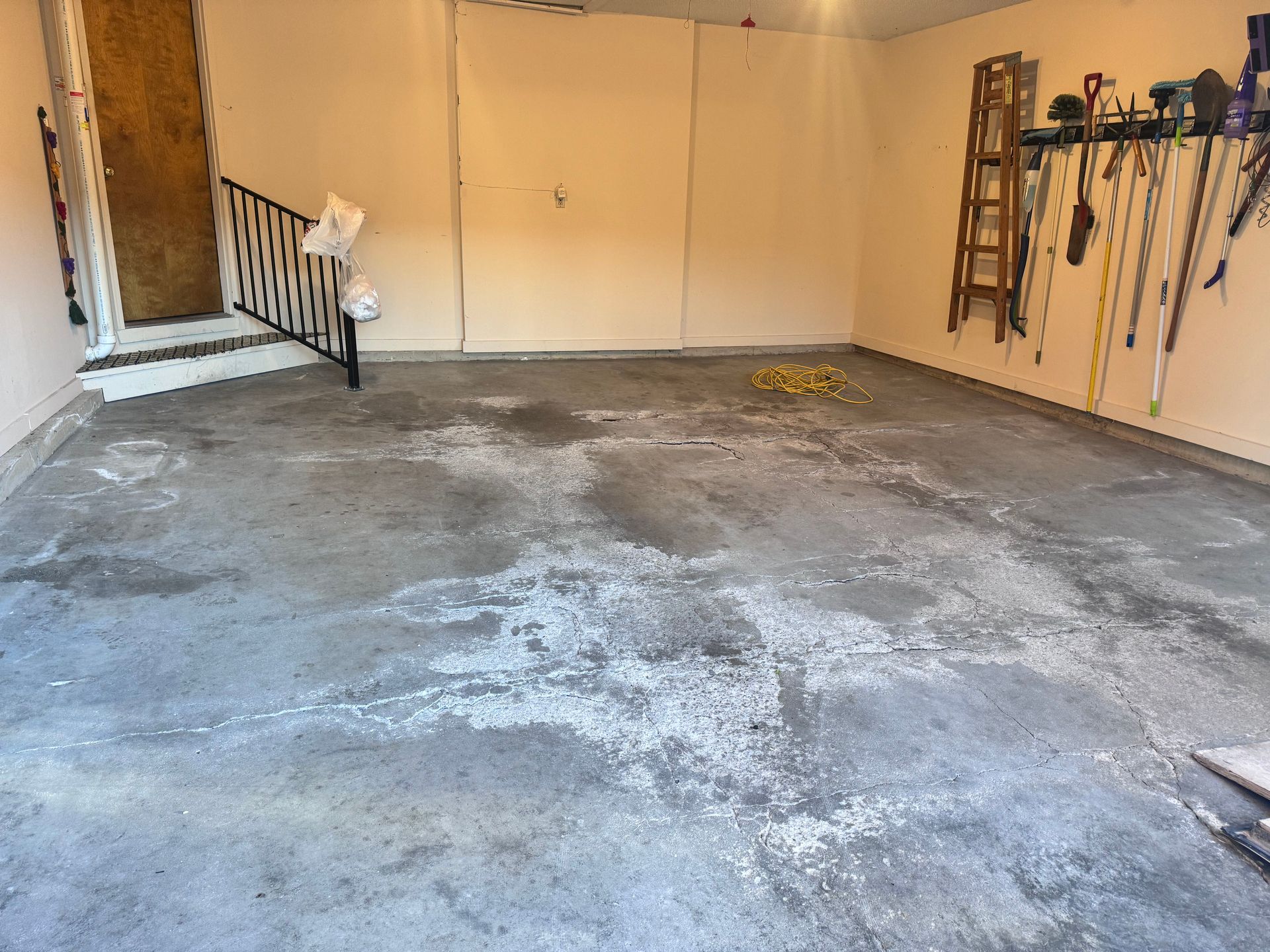 Empty garage with concrete floor, tools on the wall, and door to the left.