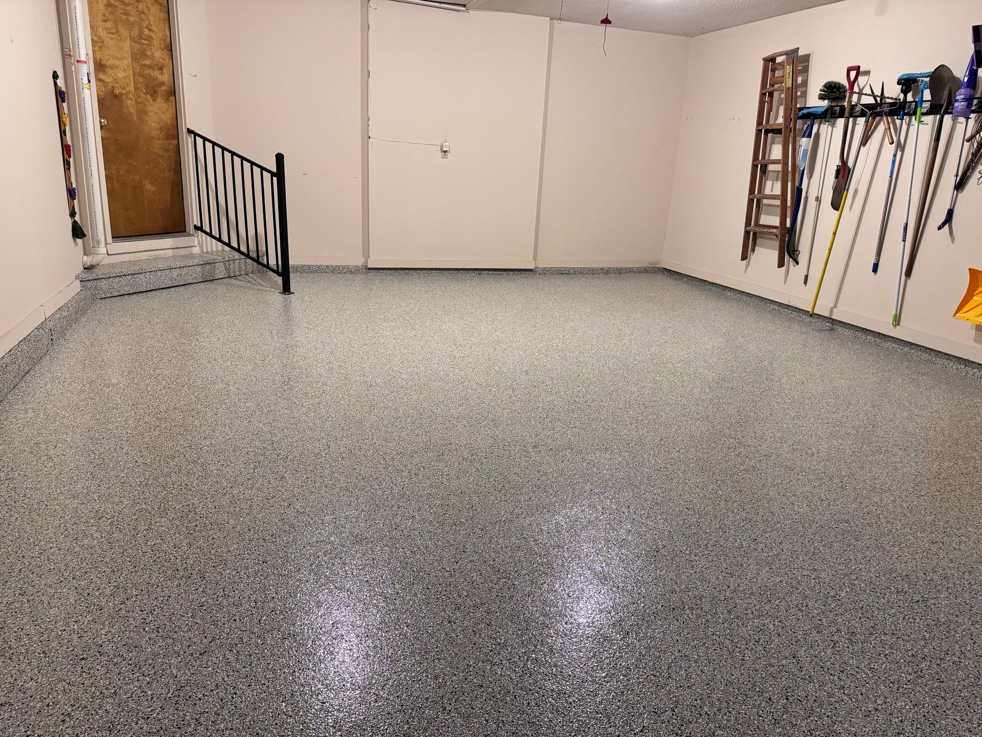 Garage with speckled epoxy floor, tools on wall, and wooden ladder.