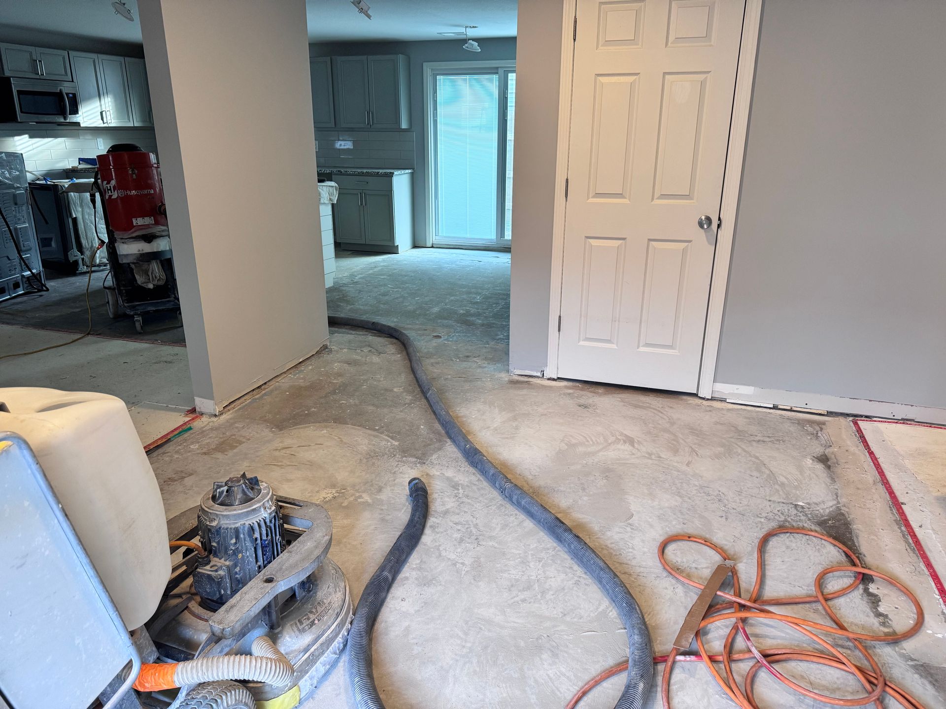 Room with flooring under renovation; grinder, hose, door, and dust visible.