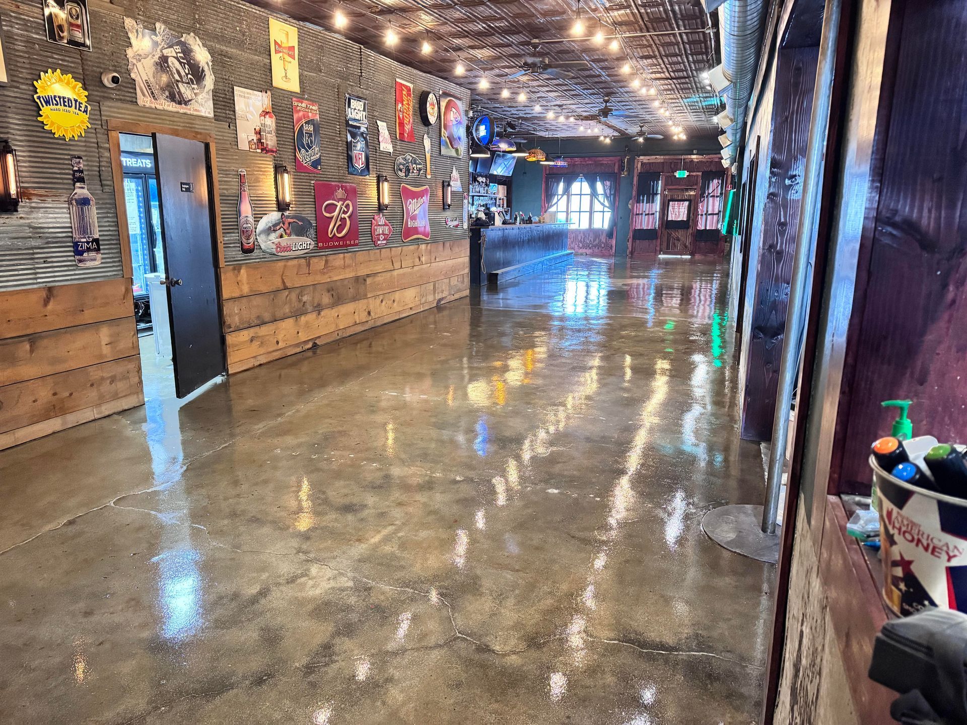 Interior of a bar with a polished concrete floor, wood paneling, string lights, and wall decor.