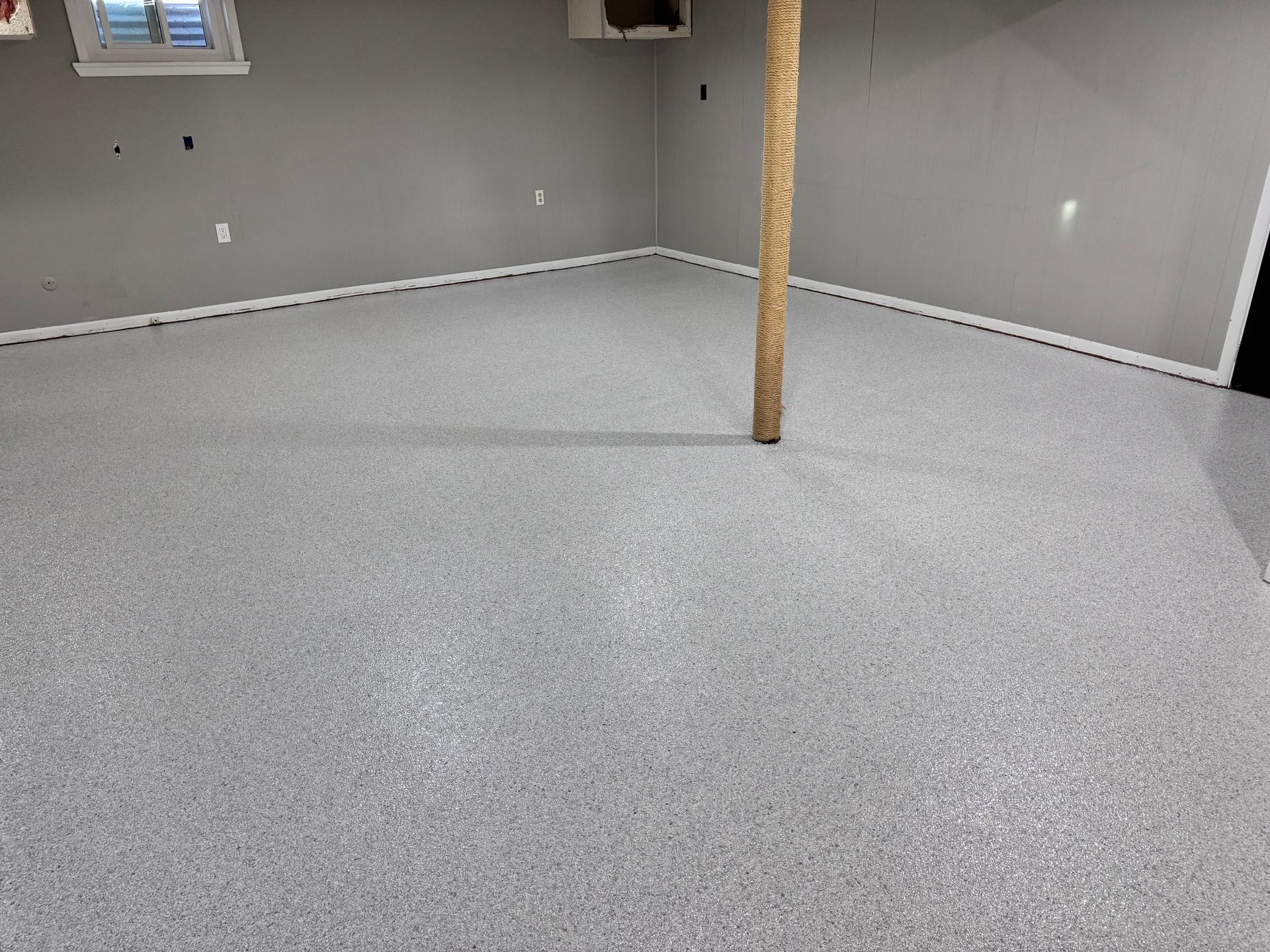 Gray epoxy flooring in a room with gray walls, a wooden support beam, and a window.