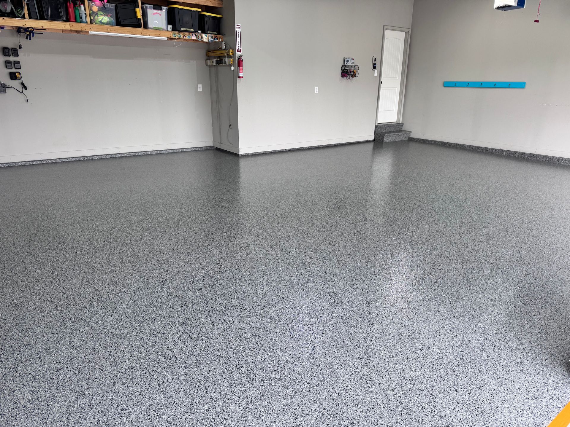 A garage with a gray speckled epoxy floor and gray walls. A door is visible in the background.