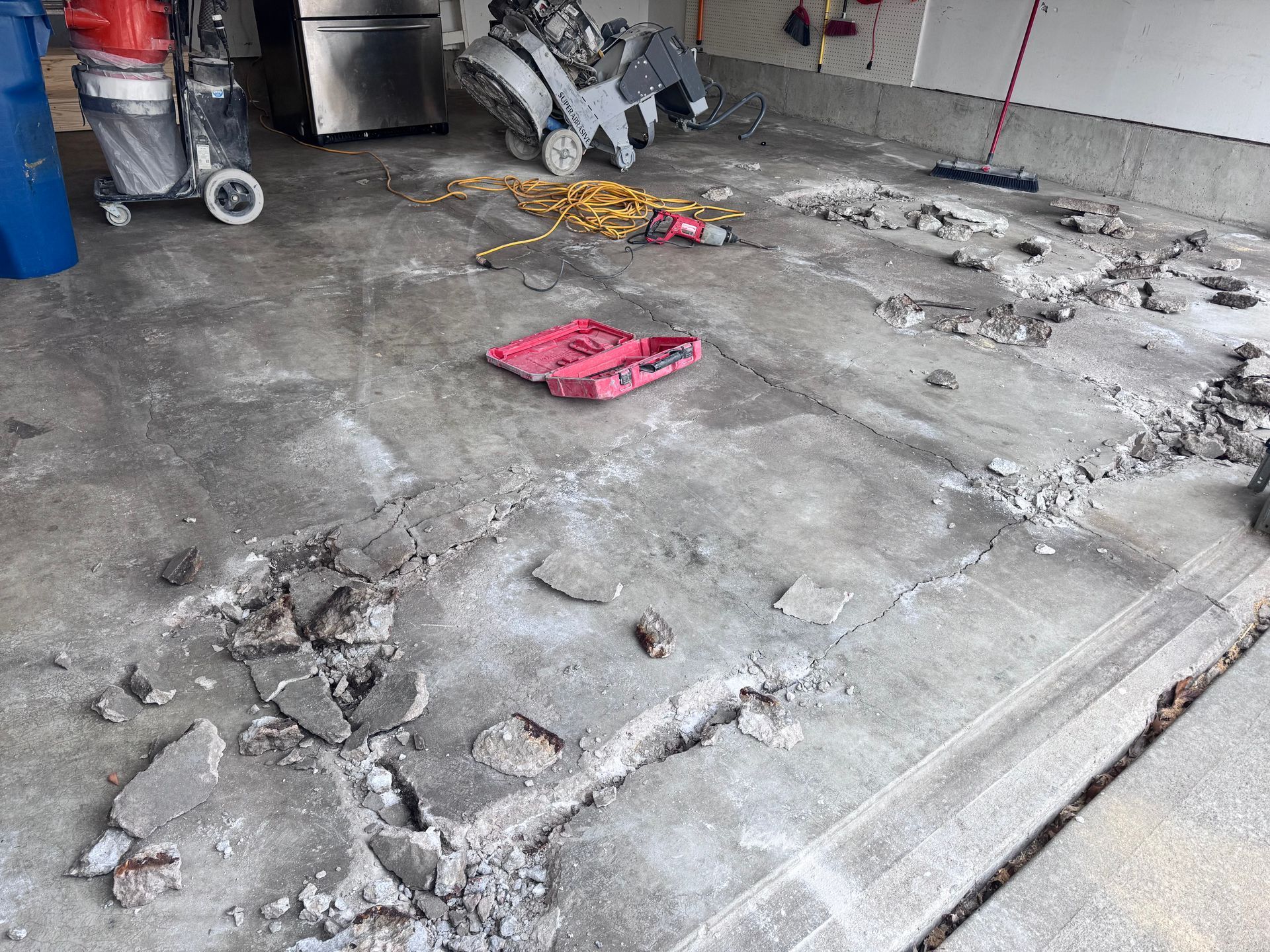 Garage concrete floor in disrepair; broken and chipped areas, tools, and equipment scattered.