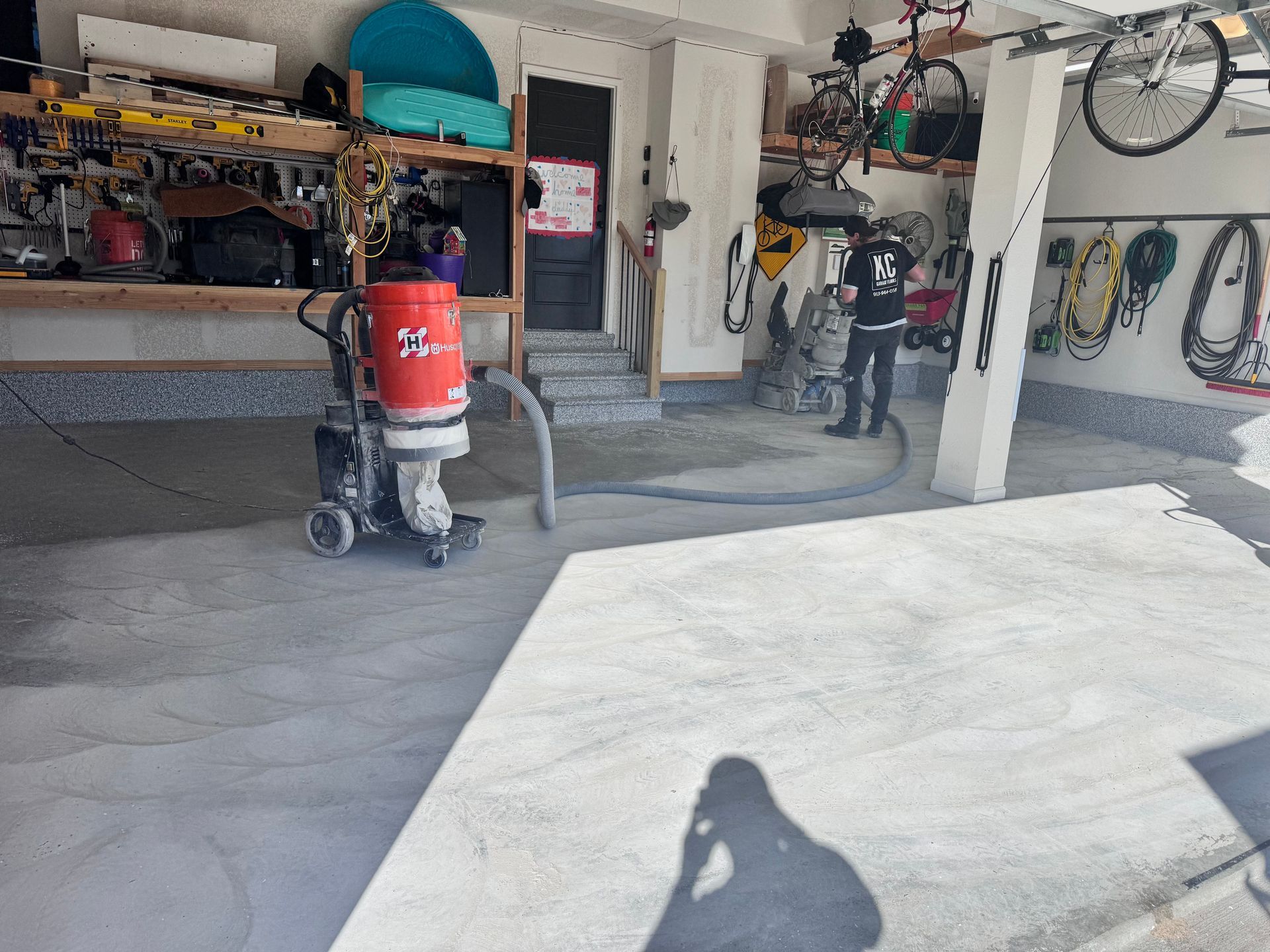Garage with concrete grinding machine in use, preparing floor. Person in dark clothing operating equipment.