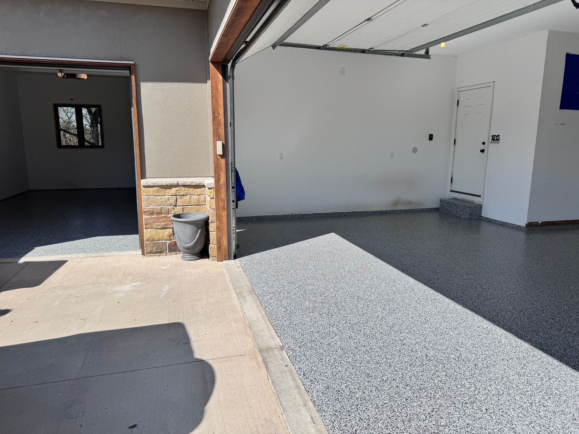 Garage interior with gray speckled epoxy flooring, open garage door, and a door leading inside.
