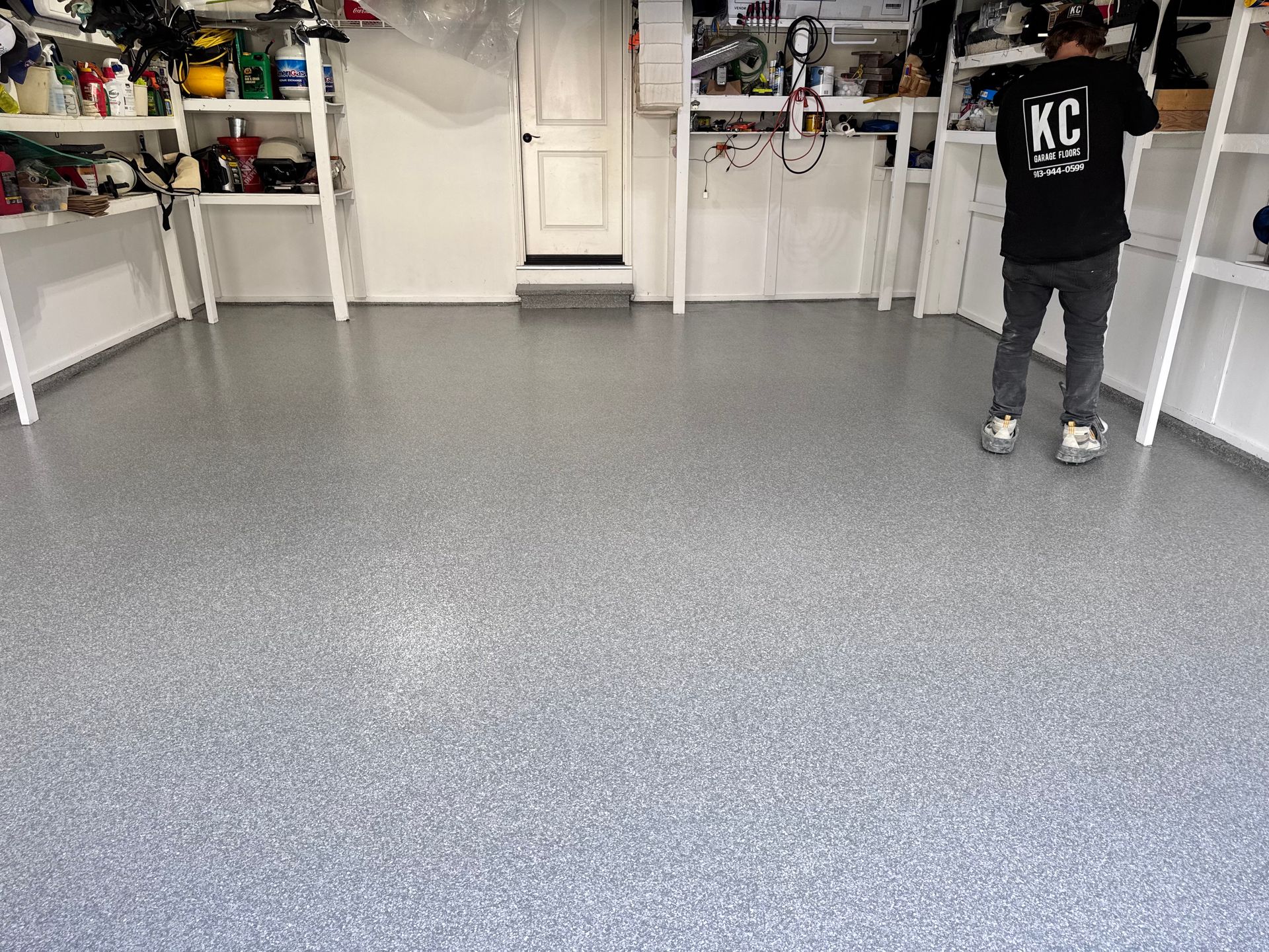 A man standing in a garage with a gray speckled epoxy floor. Shelves of items line the walls.