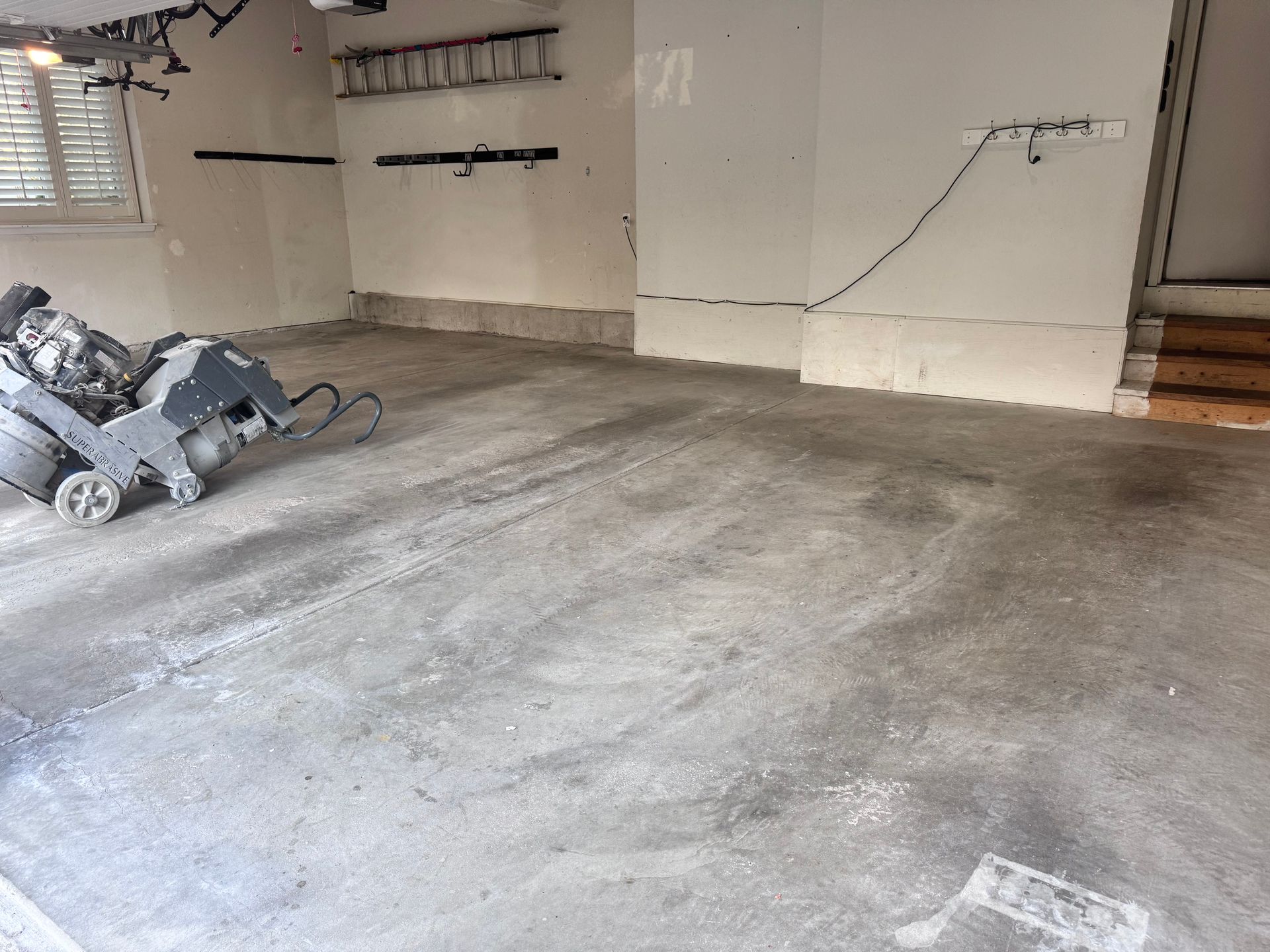 A concrete garage floor being prepared with a floor grinder.  Dust and markings are visible.