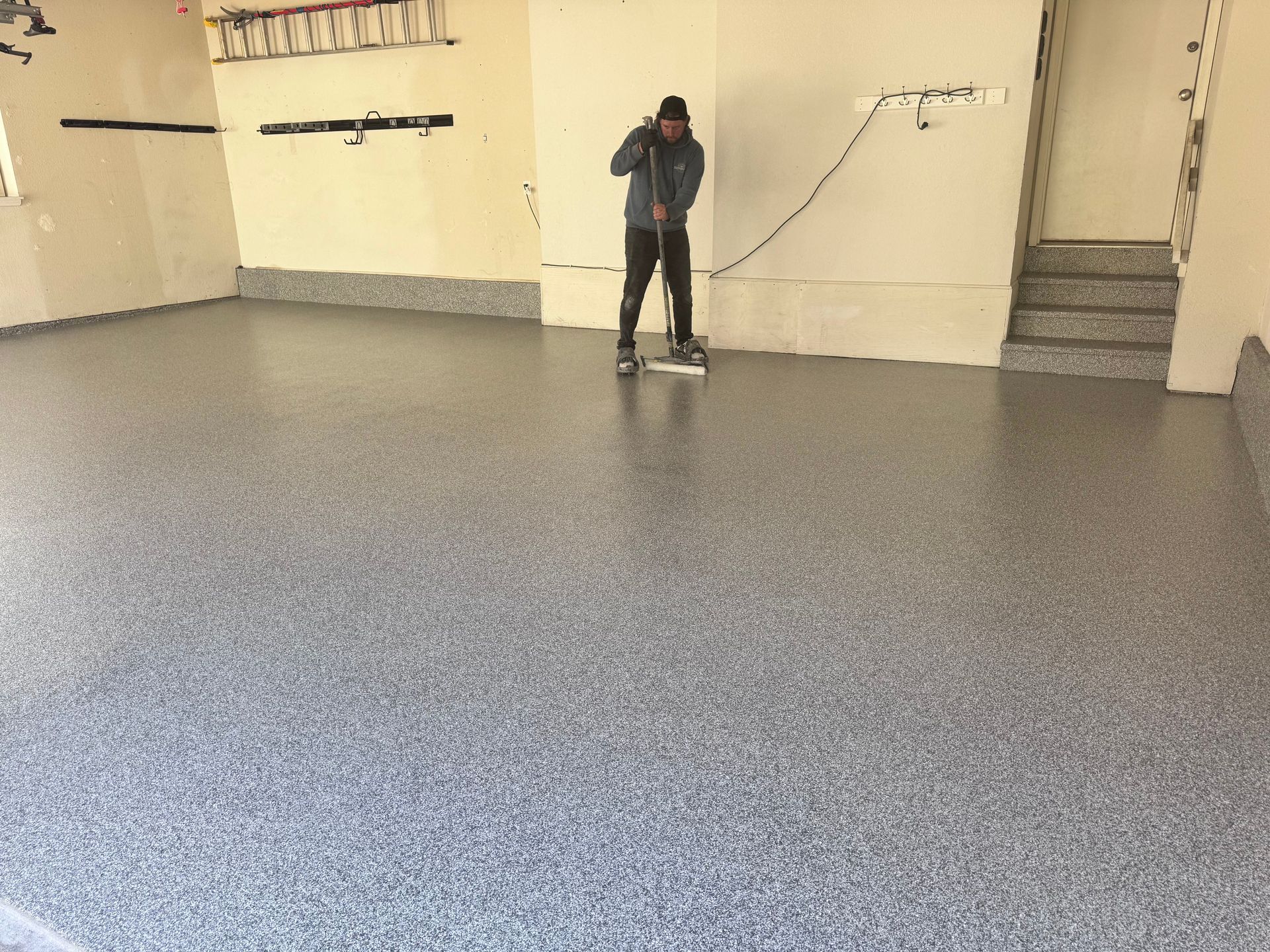 Person smoothing epoxy on a speckled gray garage floor.