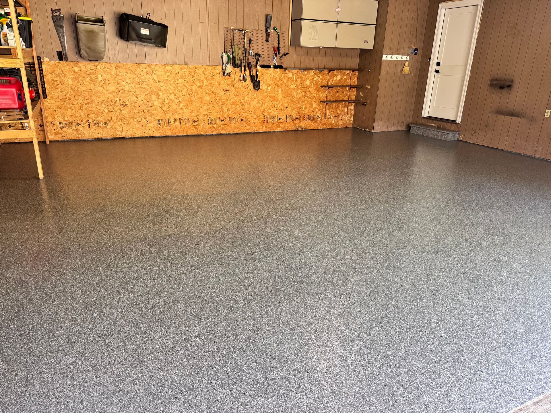 Garage with a shiny, speckled gray floor. OSB wood on the walls with tools and storage.