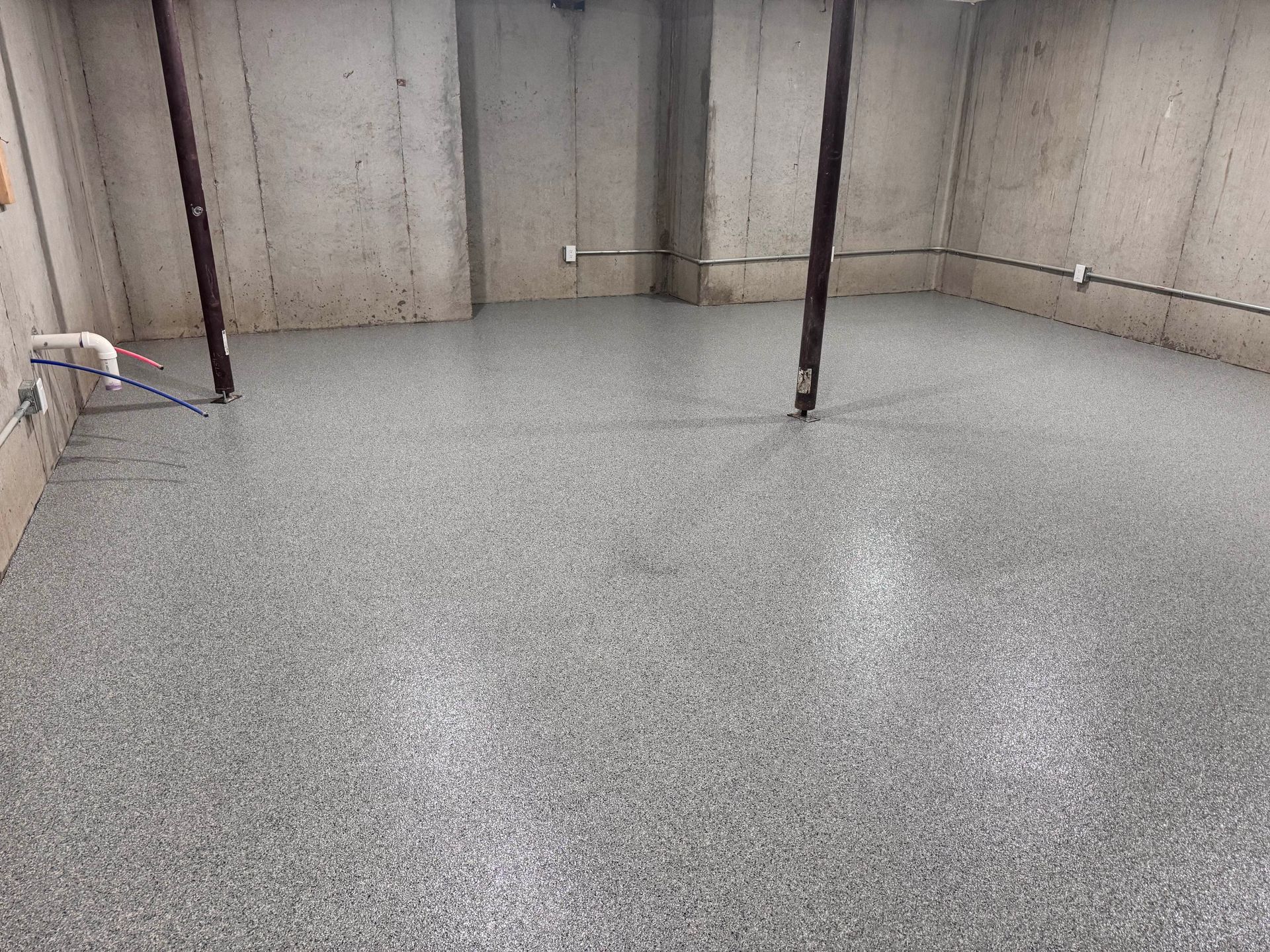 Gray speckled epoxy floor in a basement with concrete walls and support beams.