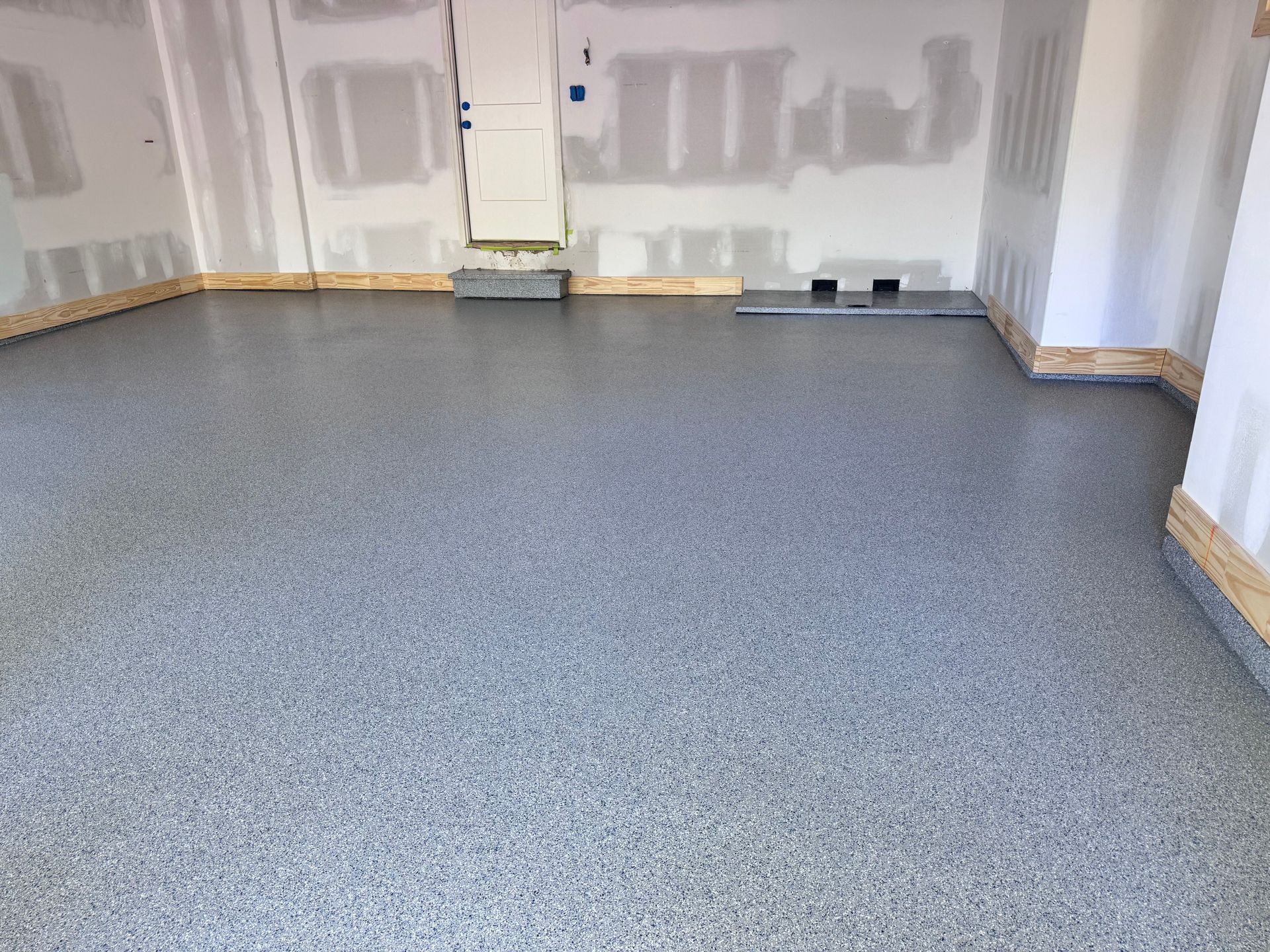Garage interior with gray speckled epoxy flooring and unfinished walls.