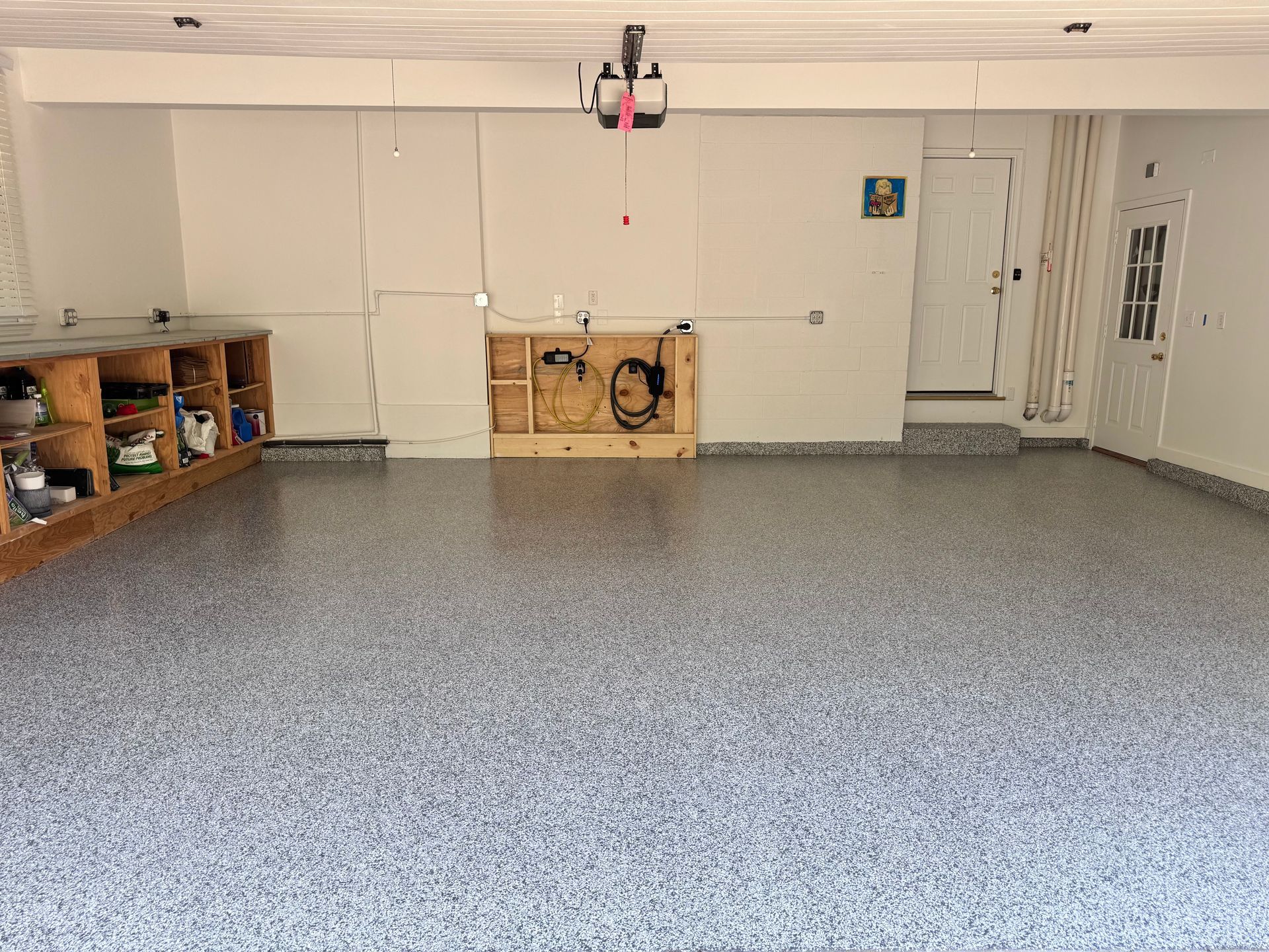 Garage interior with gray speckled floor, built-in workbench, door, and exposed wiring.